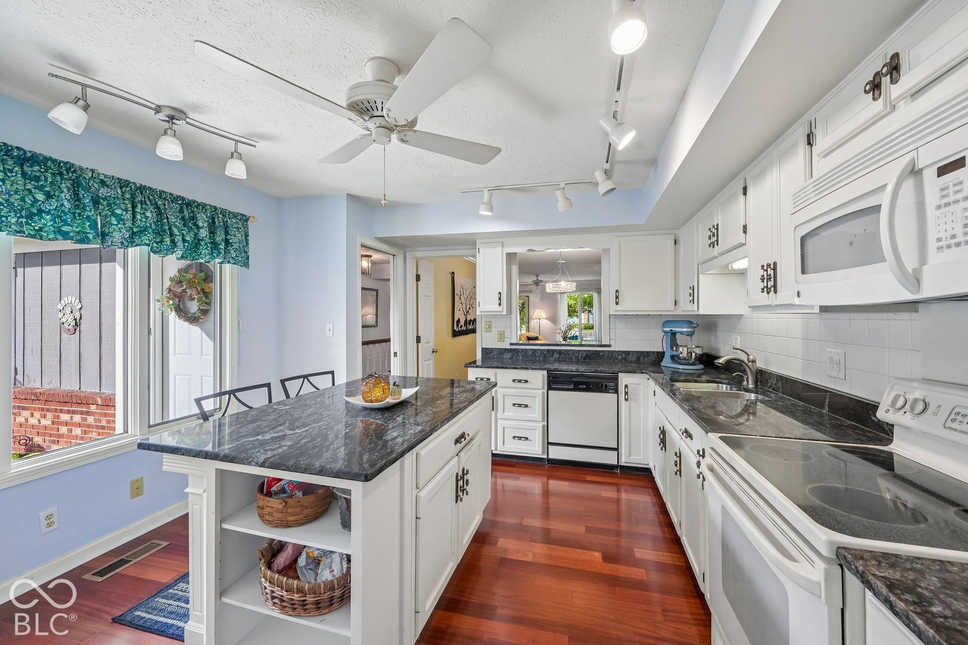 Kitchen featuring white cabinetry, dark stone countertops, wood-finish flooring, a central island with open shelving, and white appliances