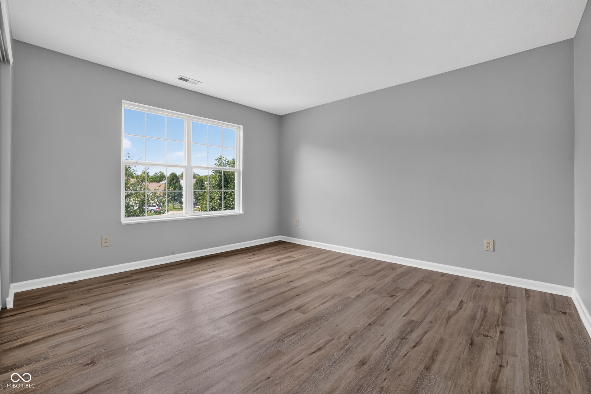 Spacious room featuring wood-finish flooring, light grey walls, and a large window