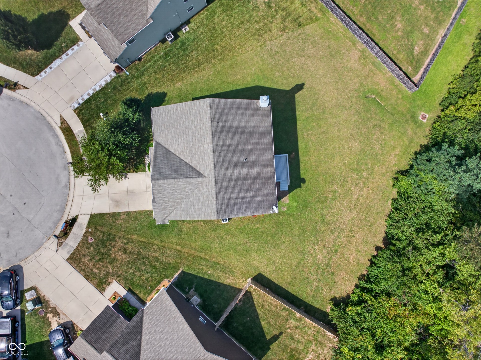 Expansive lot featuring a residential structure with a gabled roof, mature landscaping, and an adjacent paved driveway