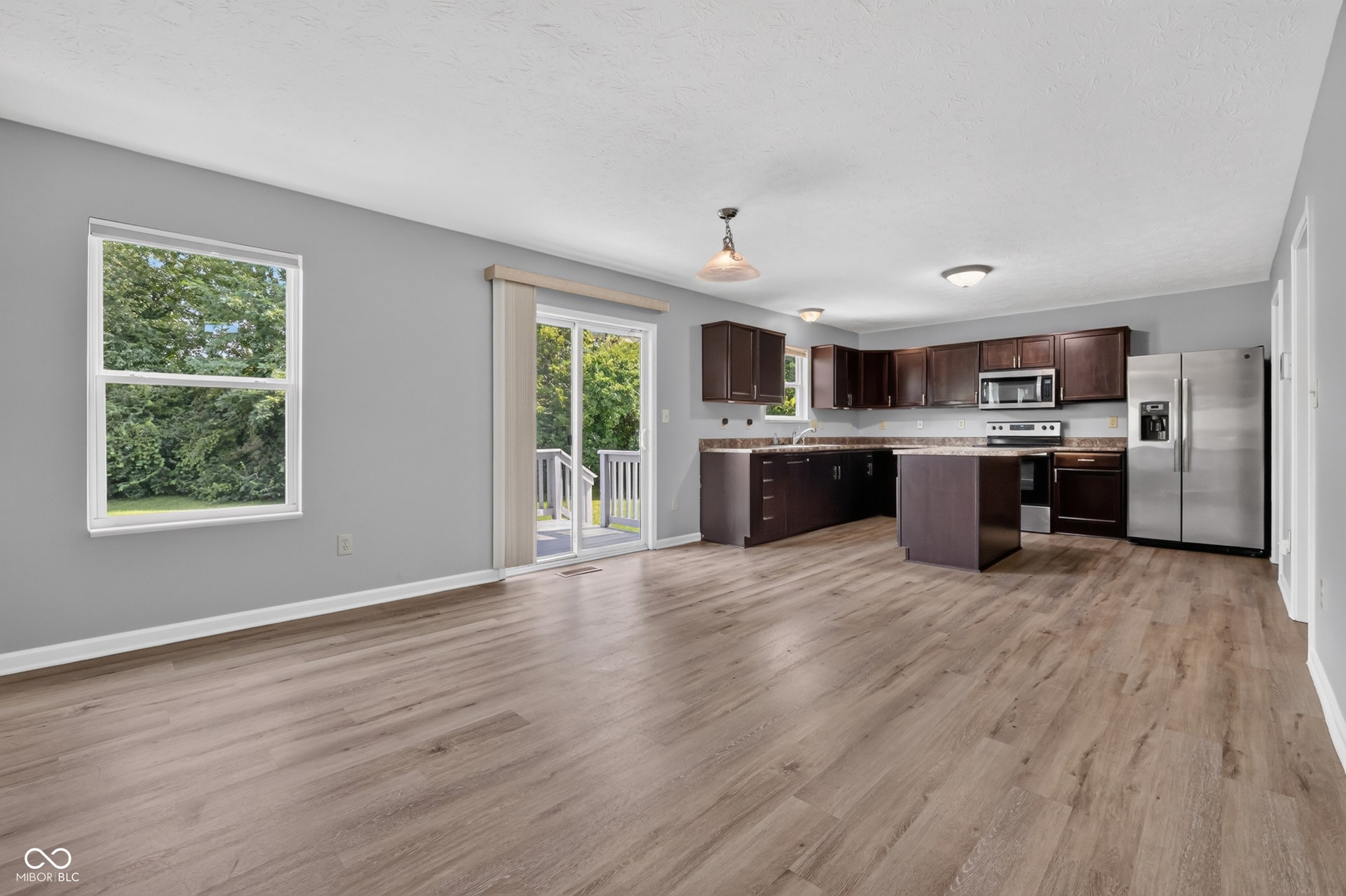 Open-concept living area with wood-finish flooring, modern kitchen island, dark wood cabinetry, stainless steel appliances, and sliding glass door access to an exterior deck