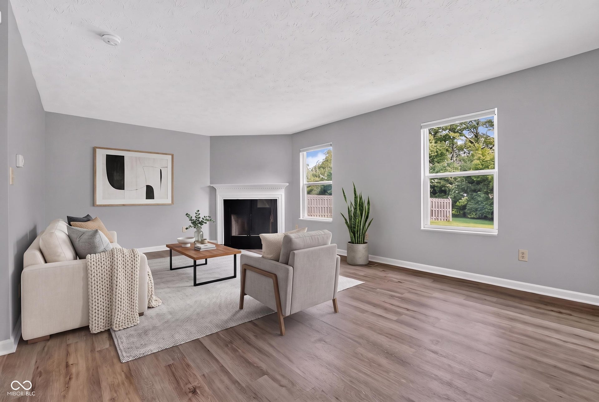 Virtually Altered - Spacious living area featuring wood-finish flooring, a white mantel fireplace, and multiple windows