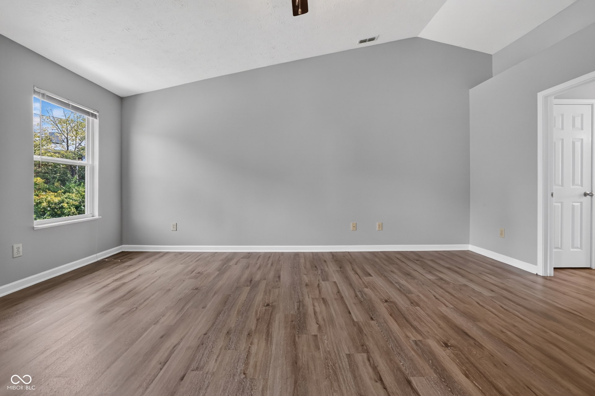 Vaulted ceiling with a ceiling fan, wood-finish flooring, and a multi-pane window
