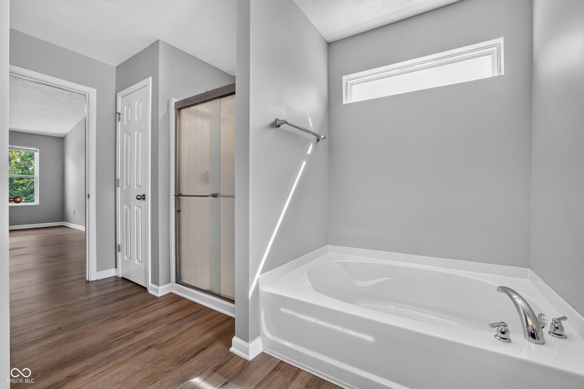 Corner soaking tub with polished chrome fixtures, separate shower with frosted glass enclosure, and wood-finish flooring