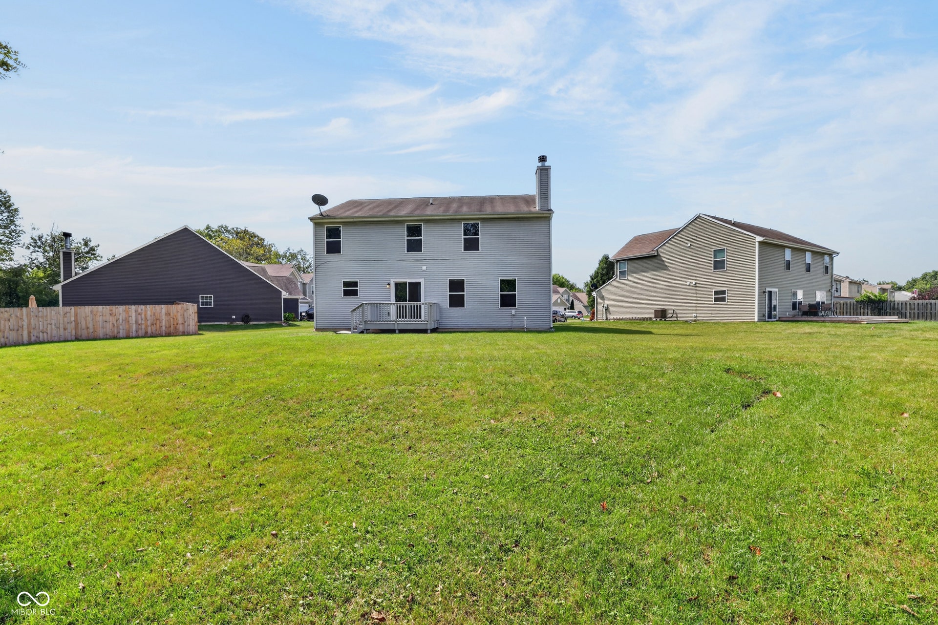 Expansive grassy yard area featuring a light-toned exterior, a wood deck, a sliding glass door, and multiple windows