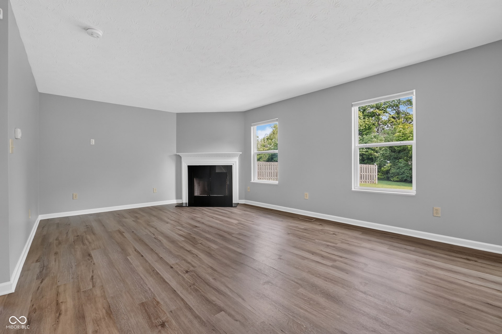 Spacious room with wood-finish flooring, a white mantel fireplace, and multiple windows