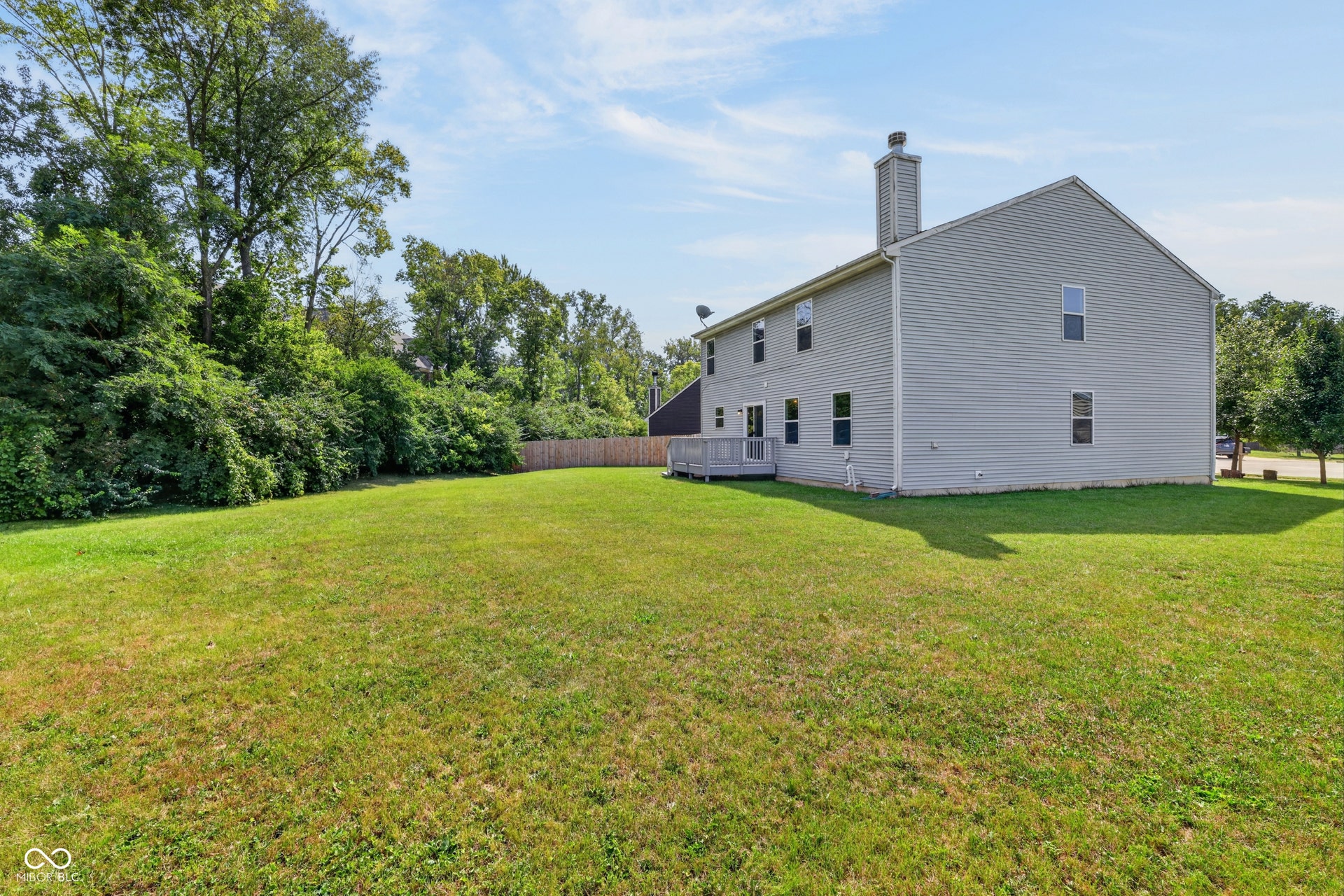 Expansive lawn with mature perimeter landscaping and a rear wood deck