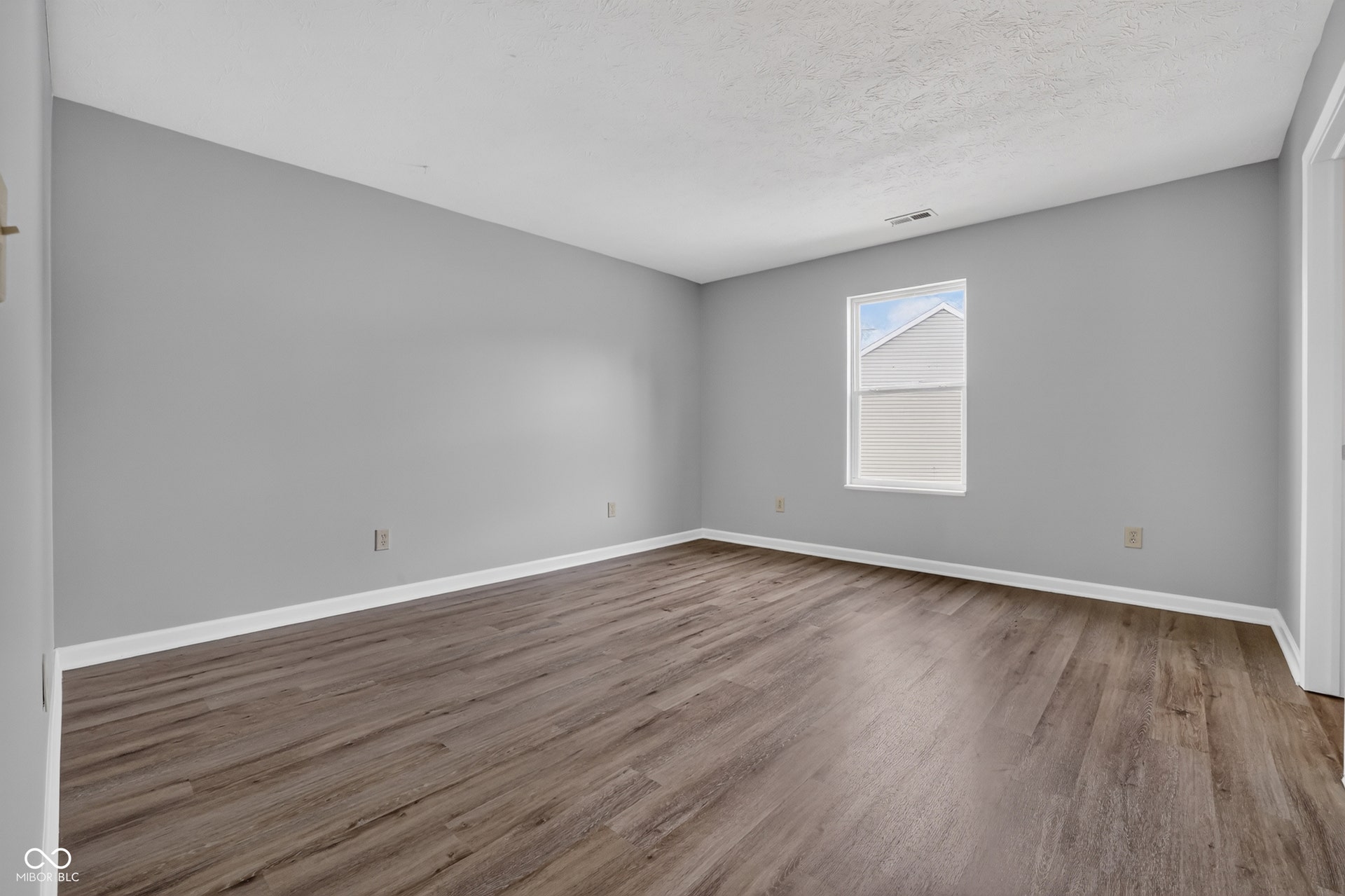 Spacious room featuring wood-finish flooring, light gray walls, white trim, and a window providing natural light