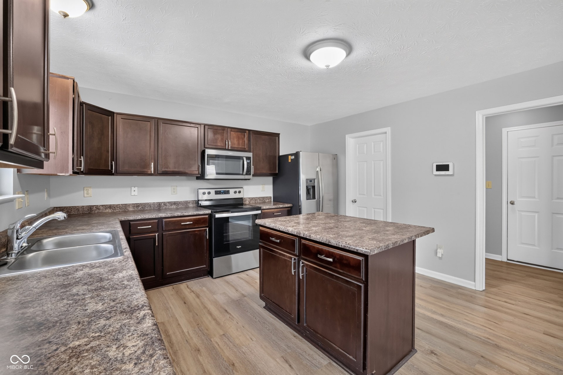 Kitchen featuring dark wood-finish cabinetry, stainless steel appliances, a center island, dual basin sink, and wood-finish flooring