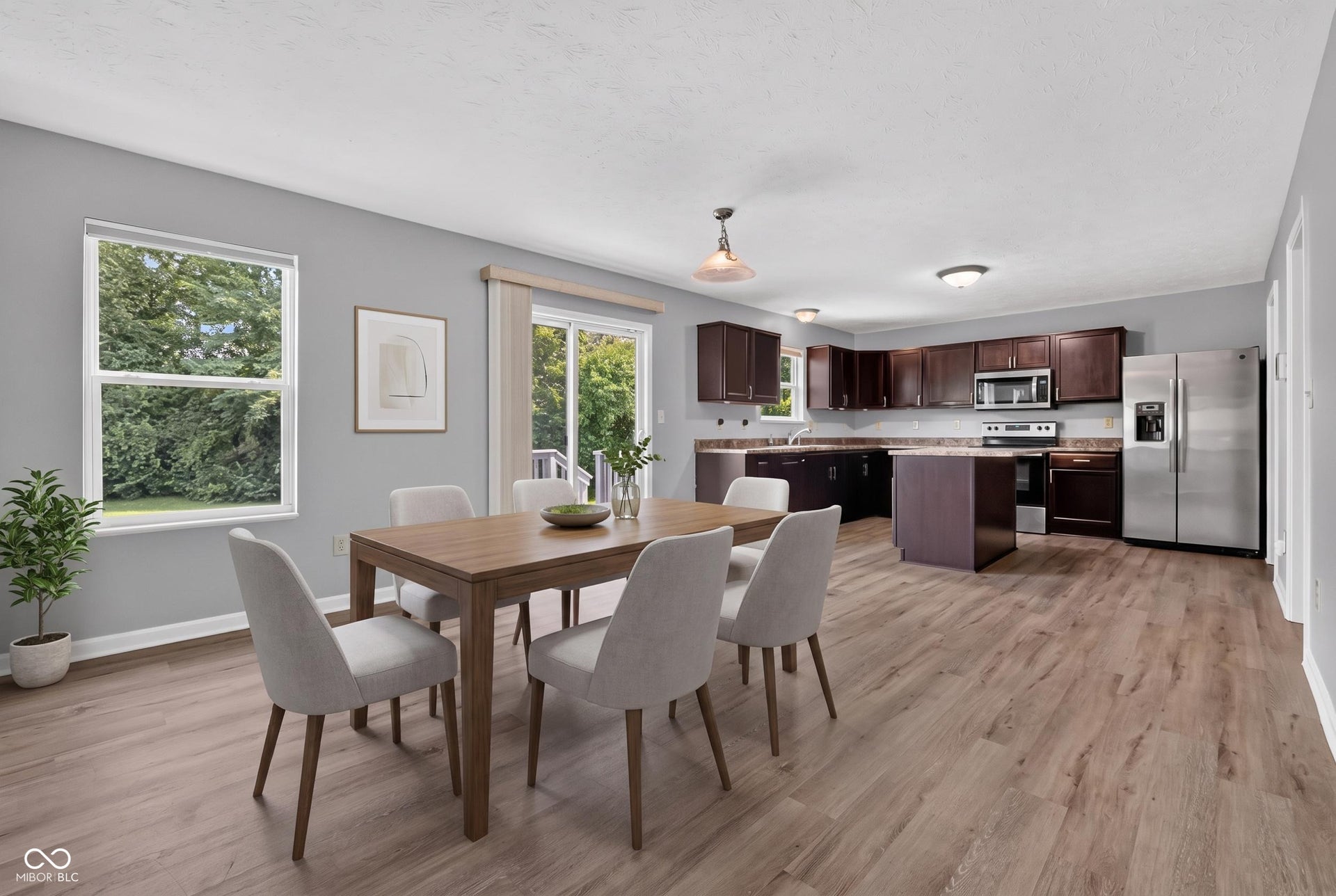 Virtually Altered - Open-concept living space with wood-finish flooring, a kitchen featuring dark wood cabinetry, a center island, and stainless steel appliances