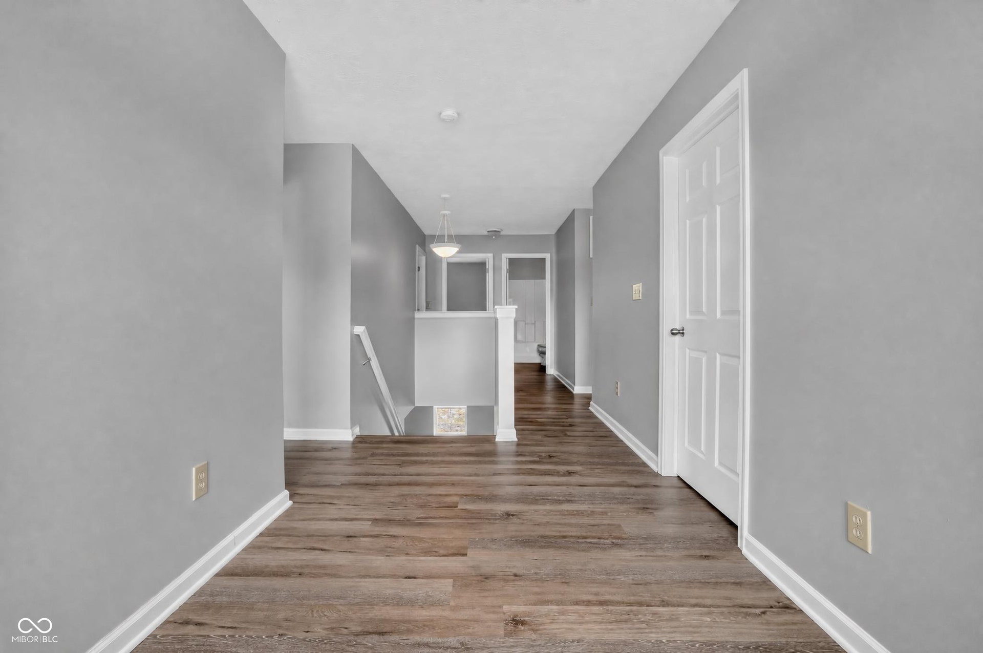 Hallway featuring wood-finish flooring, light gray wall finishes, white trim, and a white paneled door