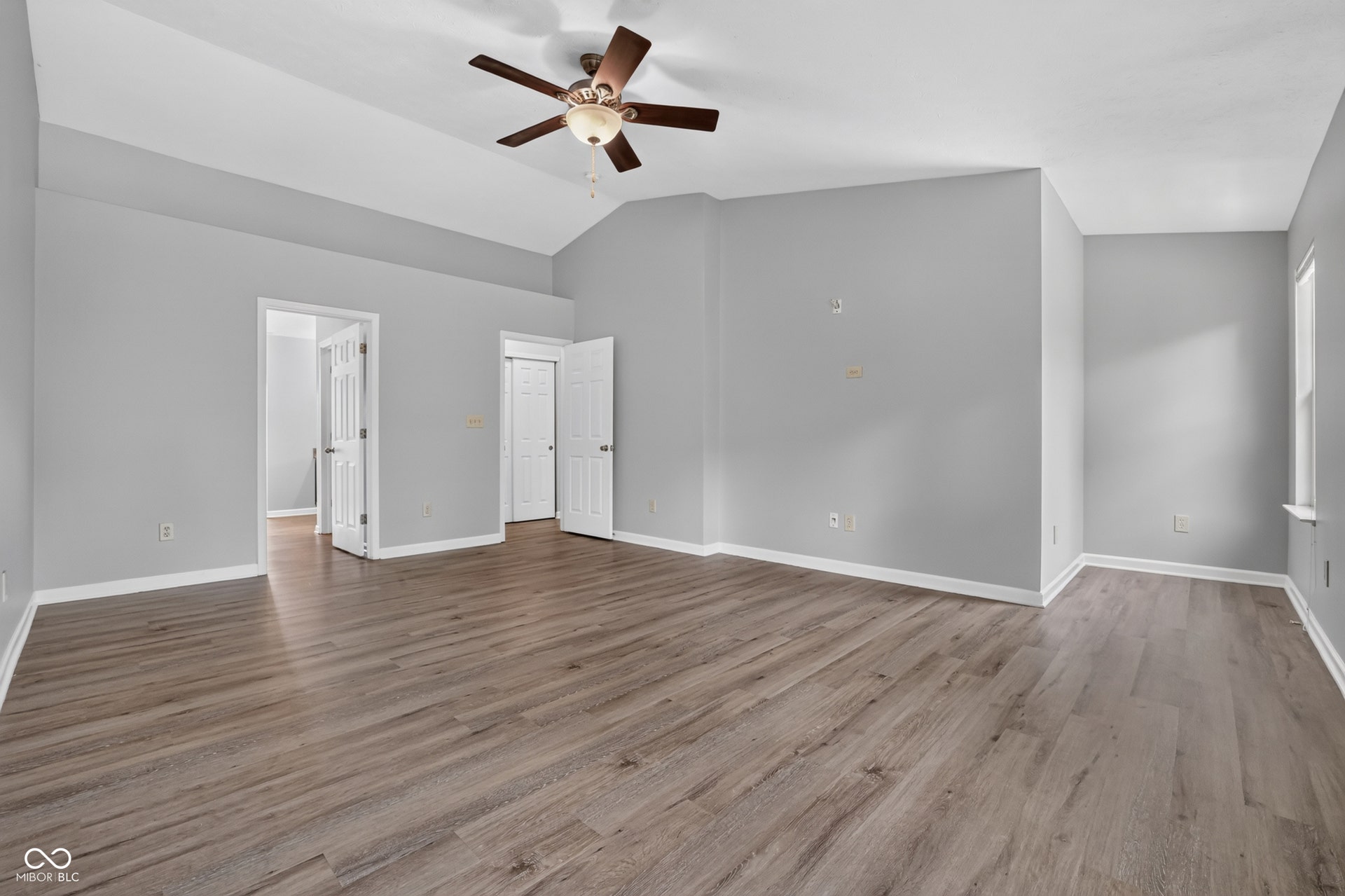 Spacious room featuring vaulted ceilings, a ceiling fan, wood-finish flooring, and white trim