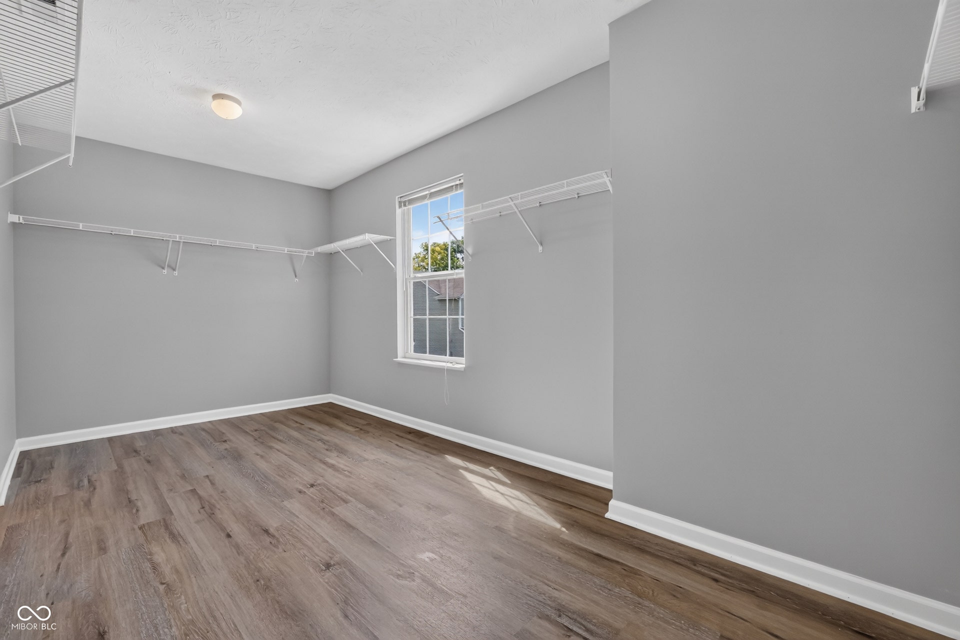 Wood-finish flooring, white wire shelving, single window, flush-mount ceiling light, and gray wall paint