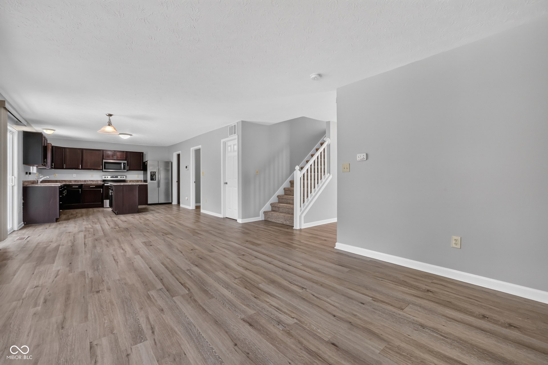 Wood-finish flooring throughout, dark wood cabinetry, black appliances, kitchen island, and a carpeted staircase with white railings
