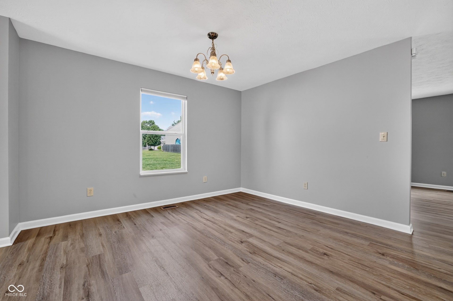 Wood-finish flooring, single pane window, gray wall paint, white trim, and a chandelier with glass shades