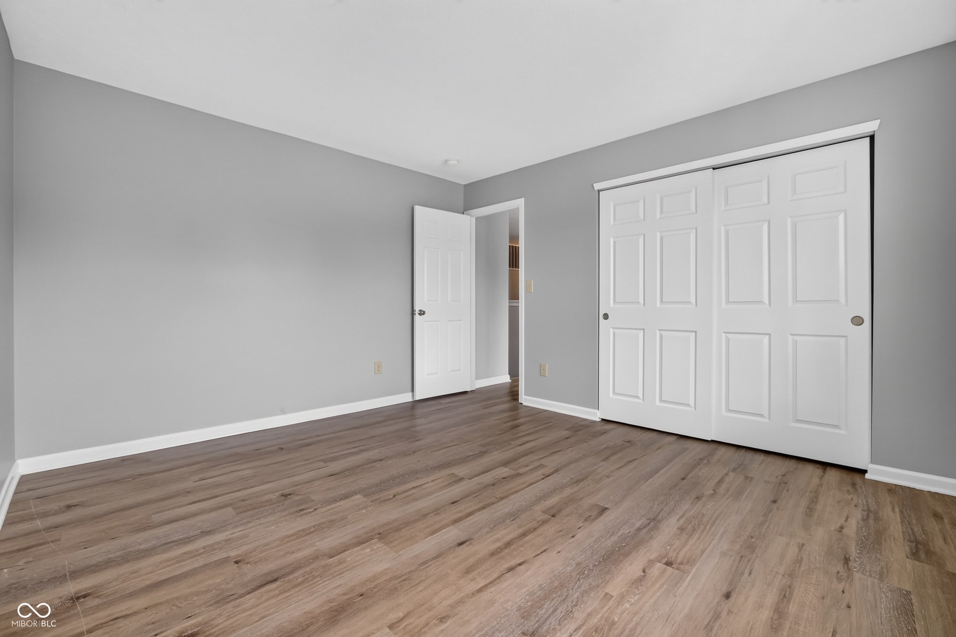 Wood-finish flooring, light grey wall paint, white trim, and a white sliding closet door