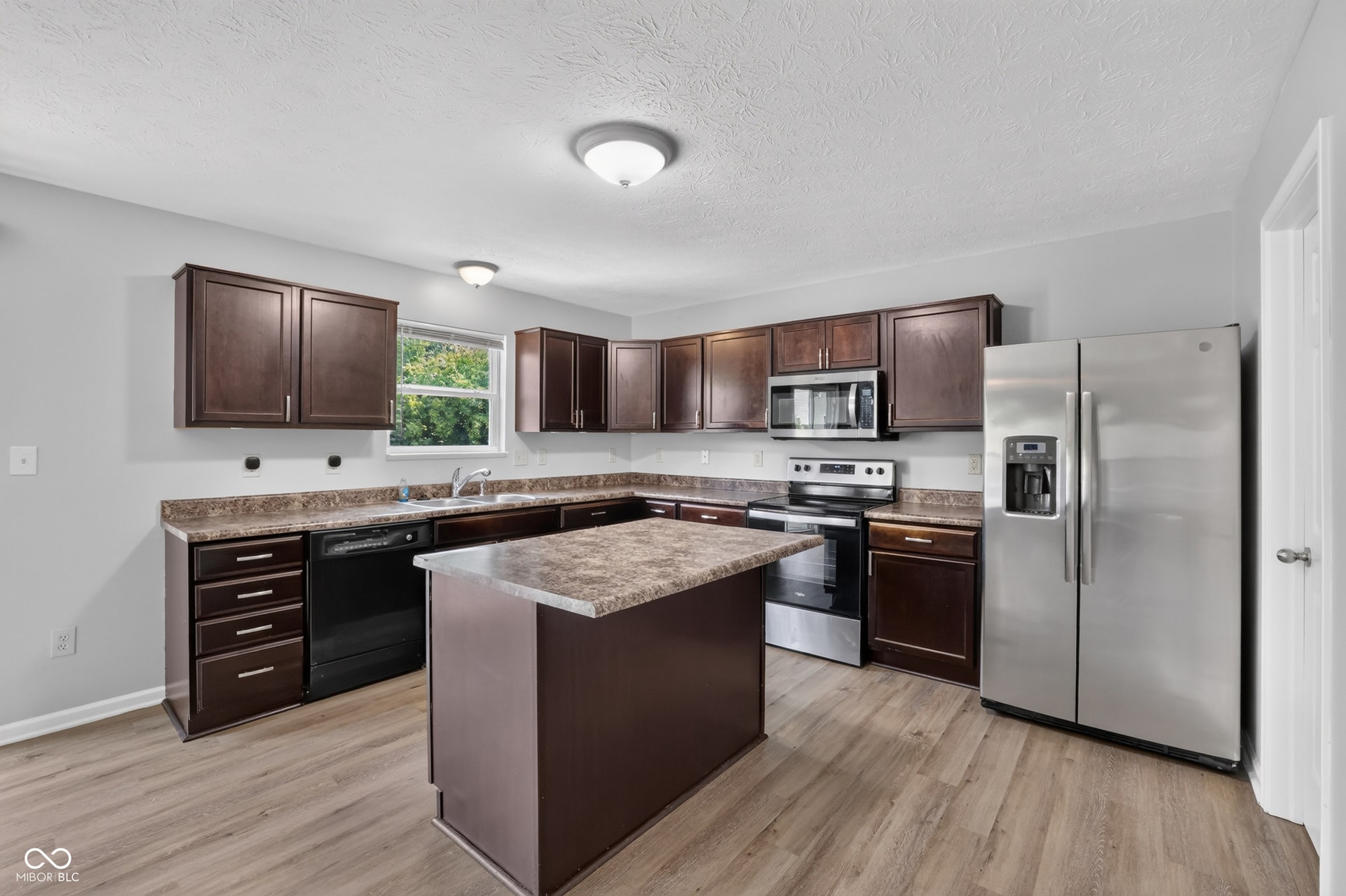 Kitchen featuring wood-finish flooring, dark wood cabinetry, a central island with a countertop, stainless steel appliances, and a window above the sink