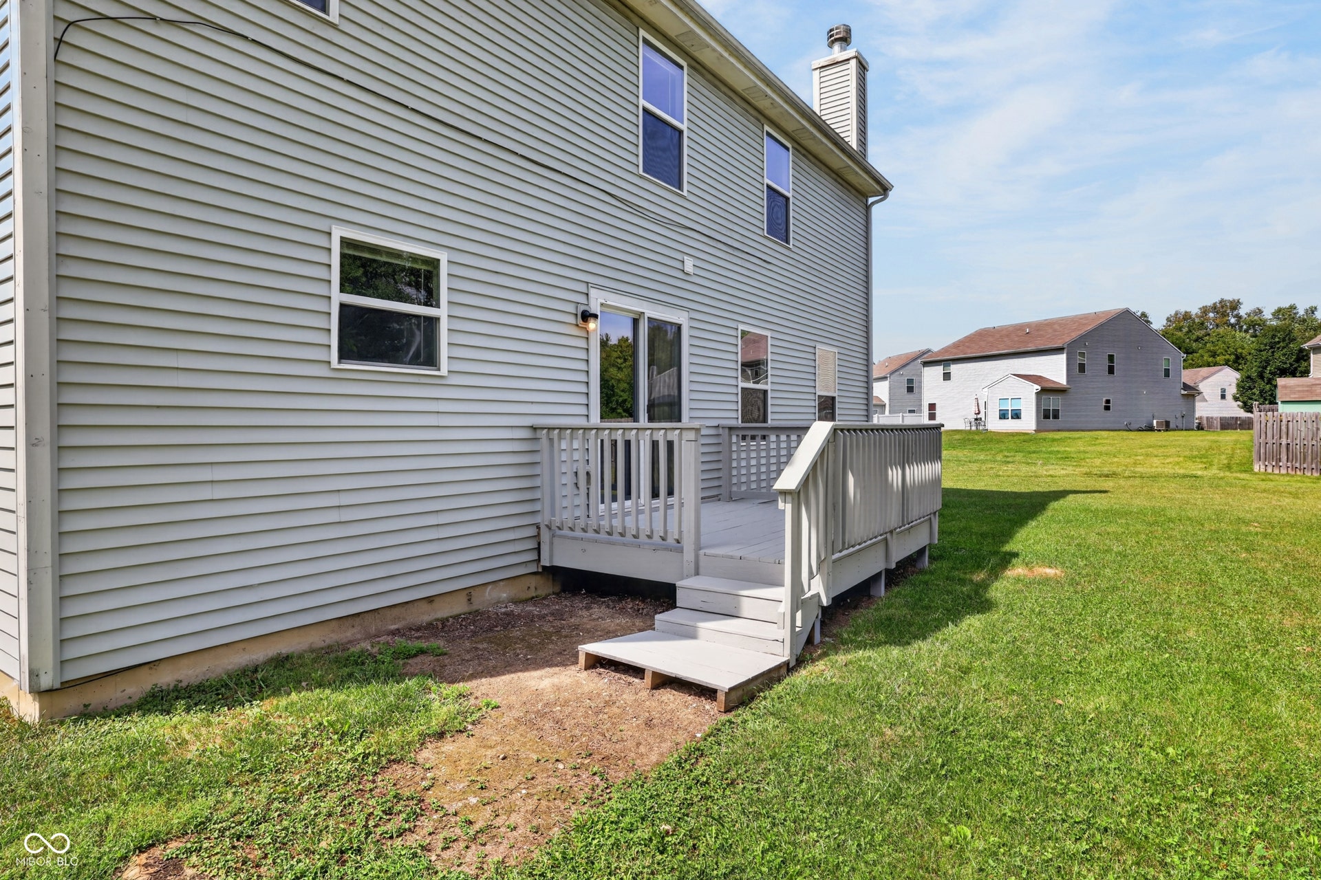 Rear exterior featuring horizontal siding, a wooden deck with railing, and expansive lawn space