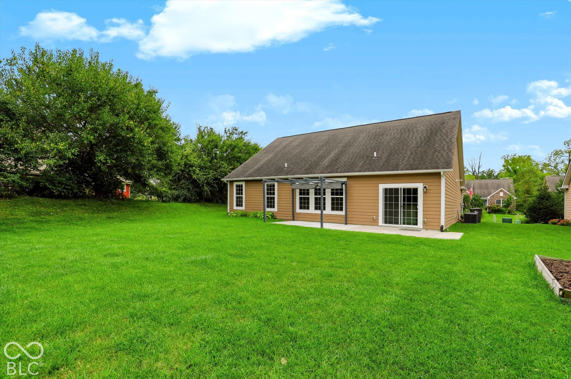 6520 Coughlan Drive, Indianapolis, IN 46278 Expansive green lawn, tan siding, white-trimmed windows, a sliding glass door, and a concrete patio with a pergola structure