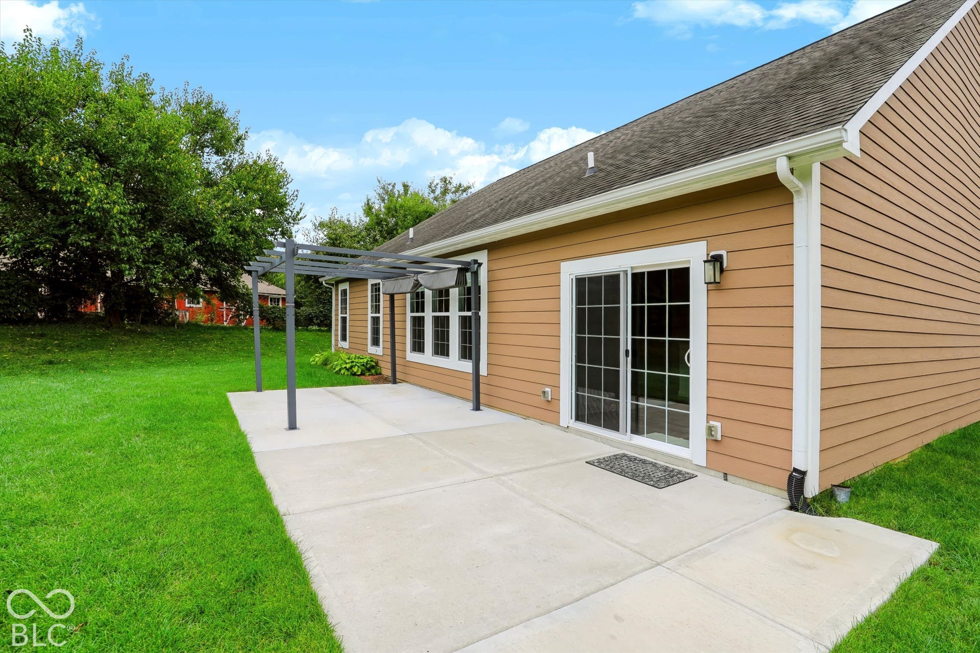 6520 Coughlan Drive, Indianapolis, IN 46278 Expansive concrete patio with pergola structure, direct access via sliding glass door, and exterior sconce lighting, all bordered by a manicured lawn
