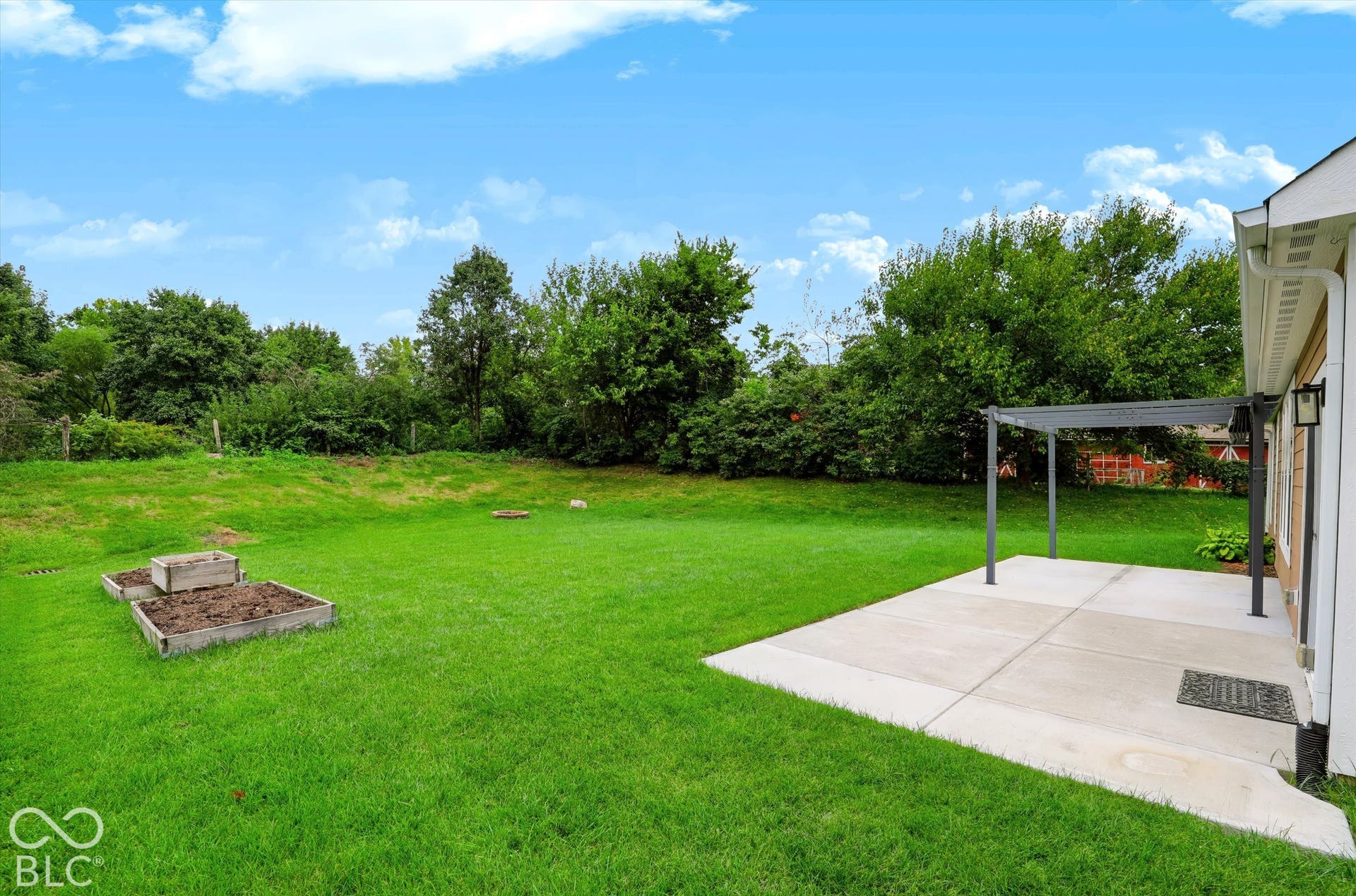 6520 Coughlan Drive, Indianapolis, IN 46278 Expansive grassy yard with mature perimeter trees, a concrete patio, and a metal pergola structure