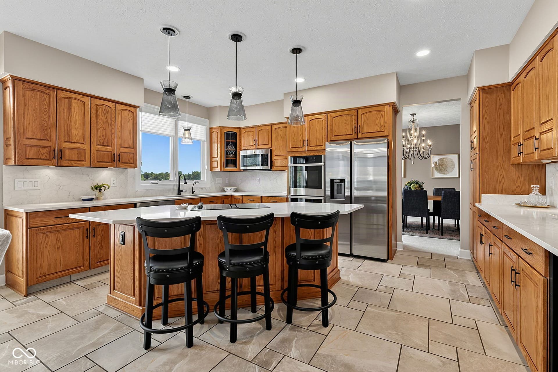 Expansive kitchen featuring wood cabinetry, stainless steel appliances, a center island with pendant lighting, vatican tile flooring, and quartz countertops.