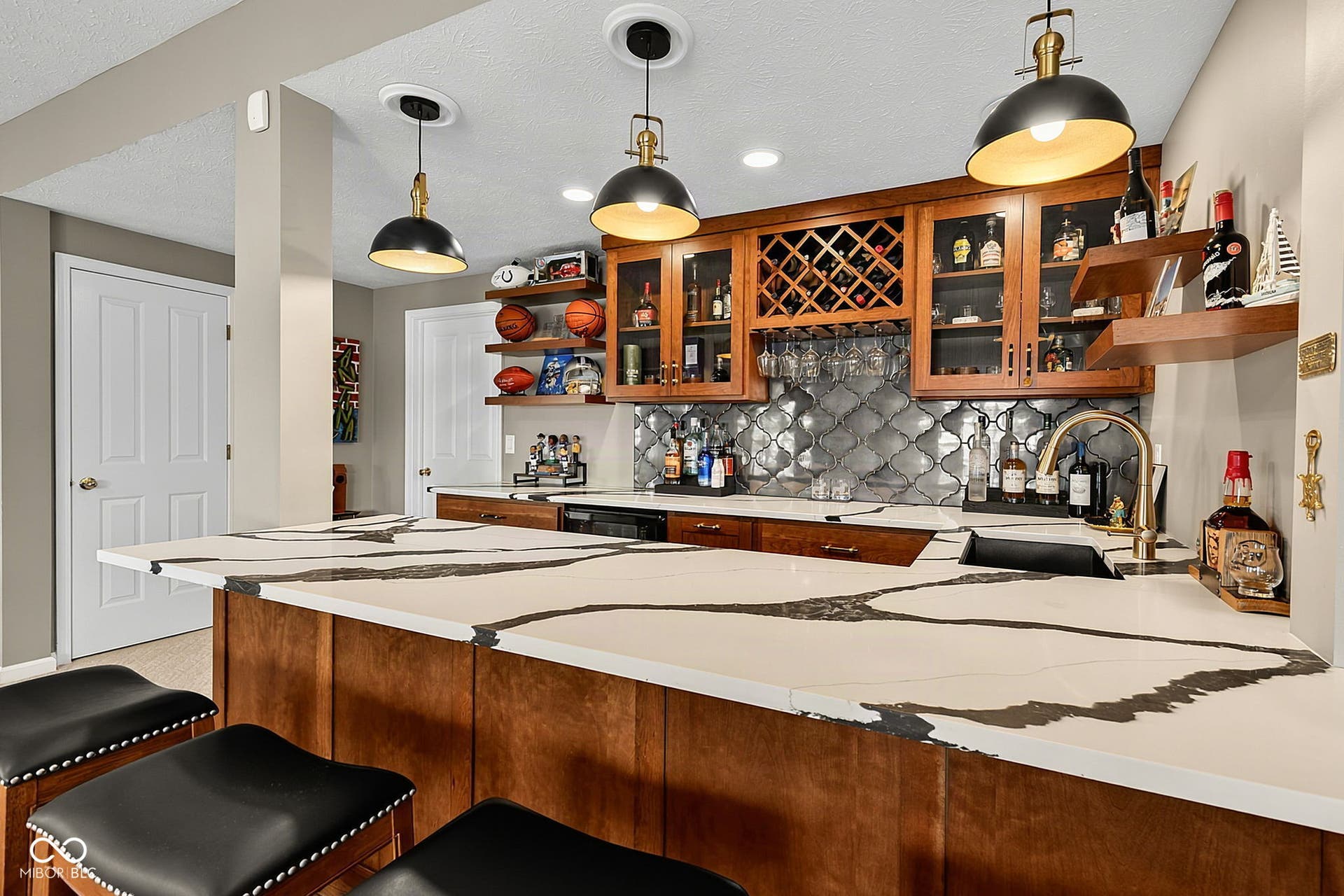 Built-in wet bar in lower level featuring custom wood cabinetry, a wine rack, and open shelving.  Large quartz countertop and seating for entertaining.