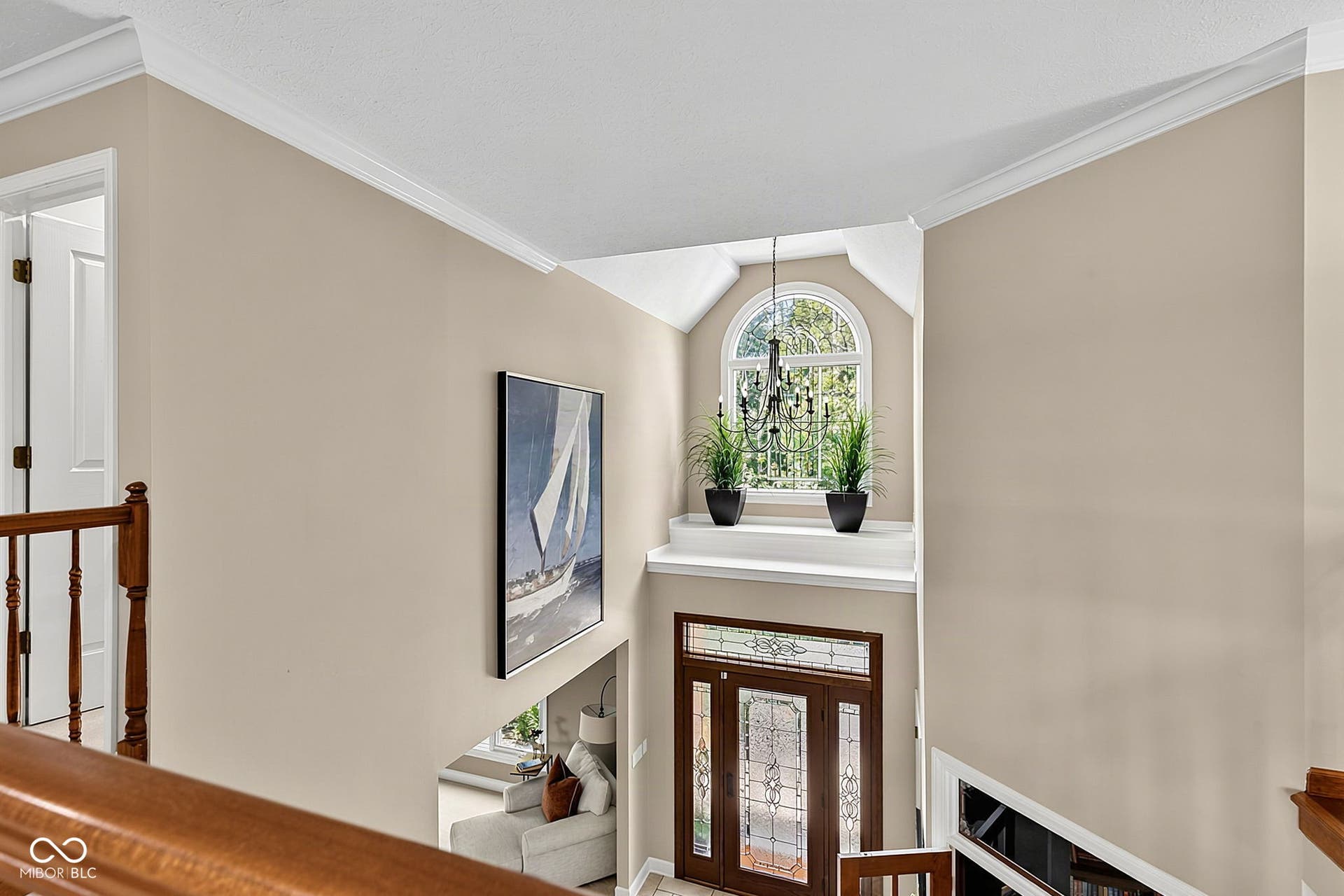Two-story foyer with decorative arched window, dark wood entry door with leaded glass accents.