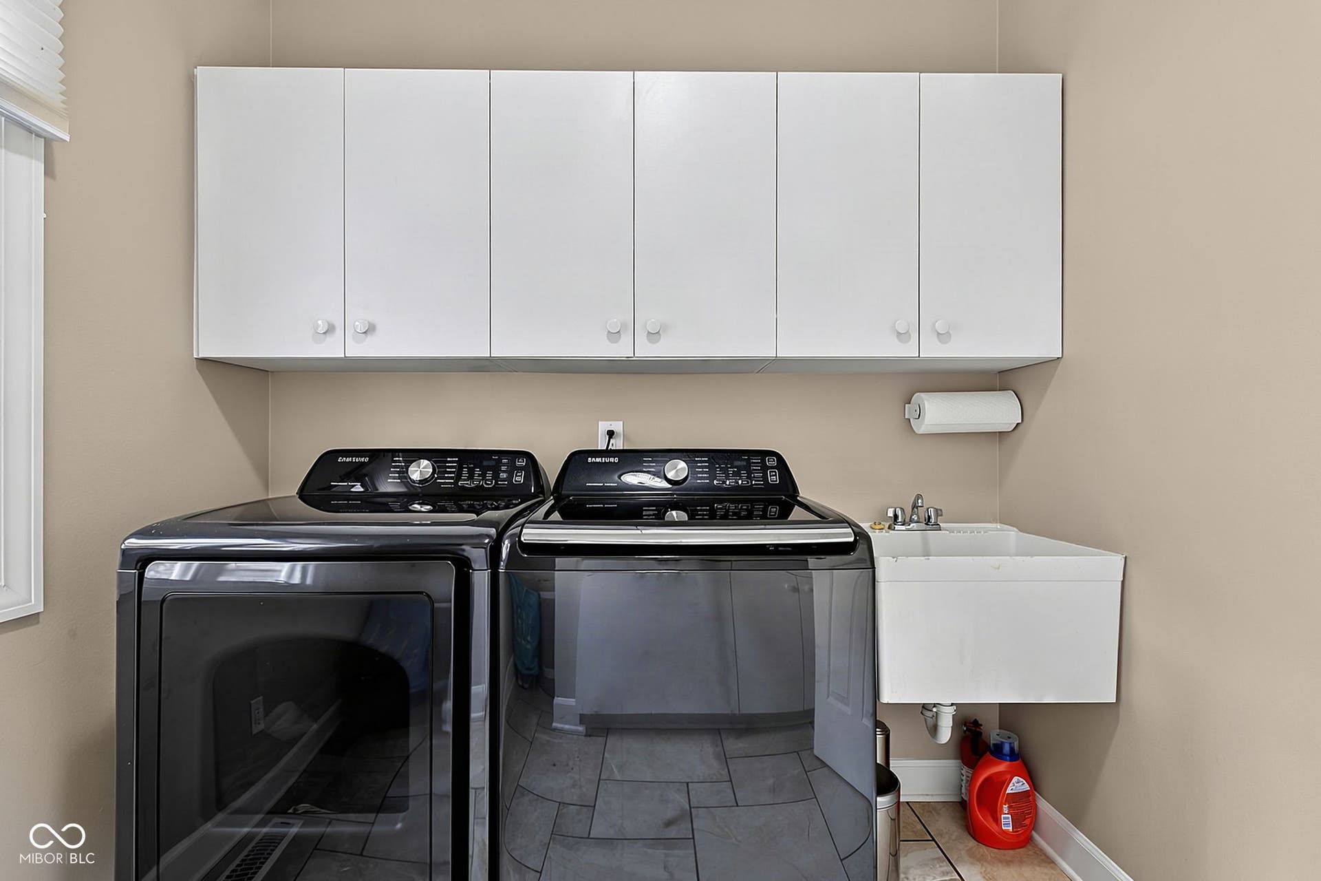 White cabinetry, utility sink with chrome faucet, and tile flooring.