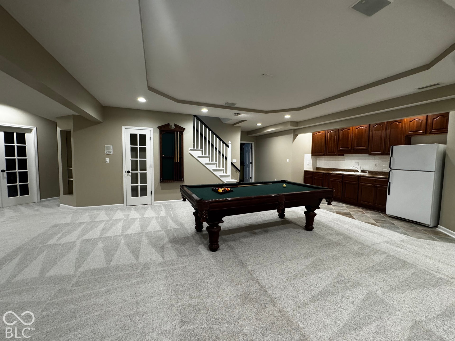 Recessed lighting, tray ceiling, staircase with white risers and dark handrail, French doors, and built-in cabinetry with a sink