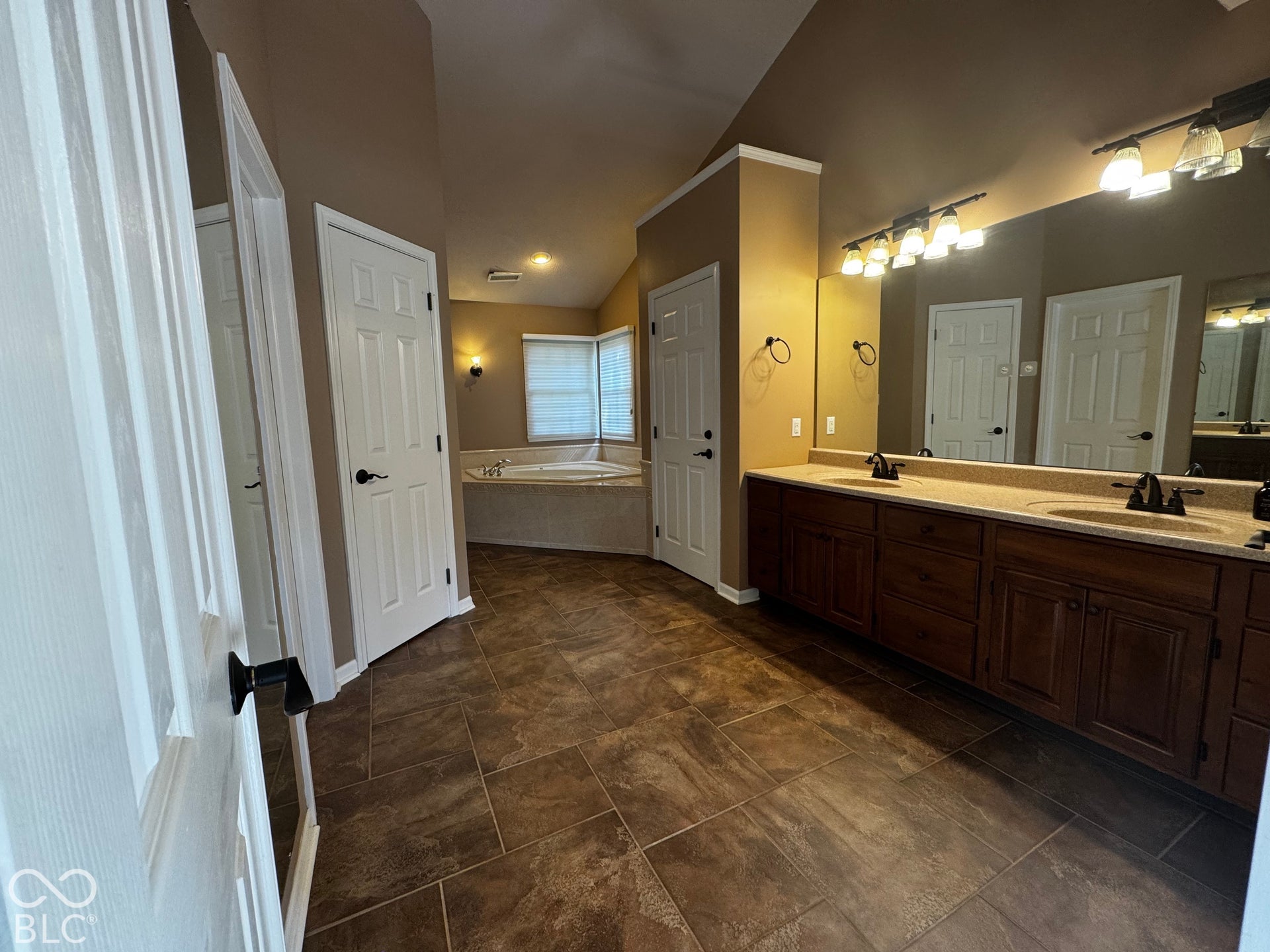 Expansive tiled flooring leads to a large soaking tub, a double vanity with ample counter space, and a wall-mounted mirror
