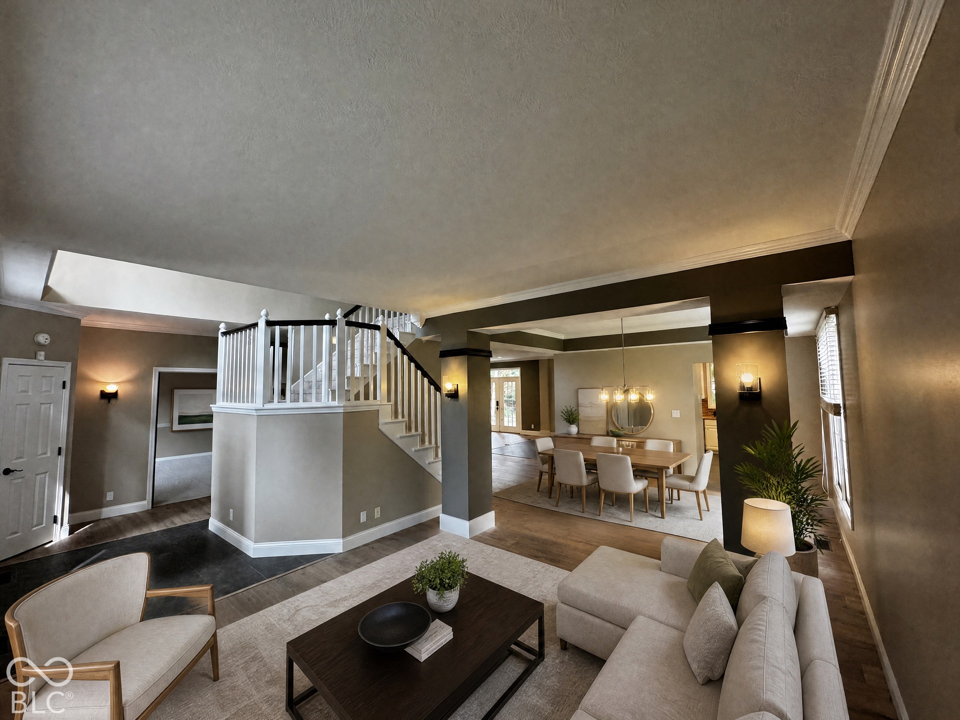 Virtually Altered - Open-concept interior featuring wood-finish flooring, a prominent staircase with white balusters and dark handrails, and crown molding