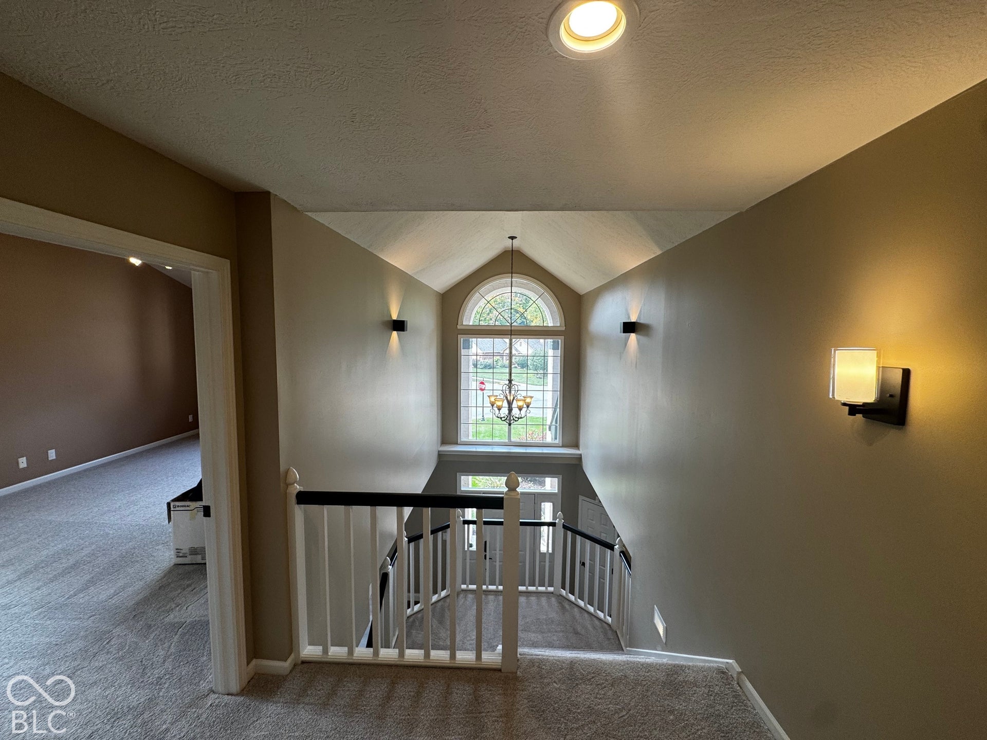 Vaulted ceiling with an arched window, decorative chandelier, and staircase with white spindles and a black handrail