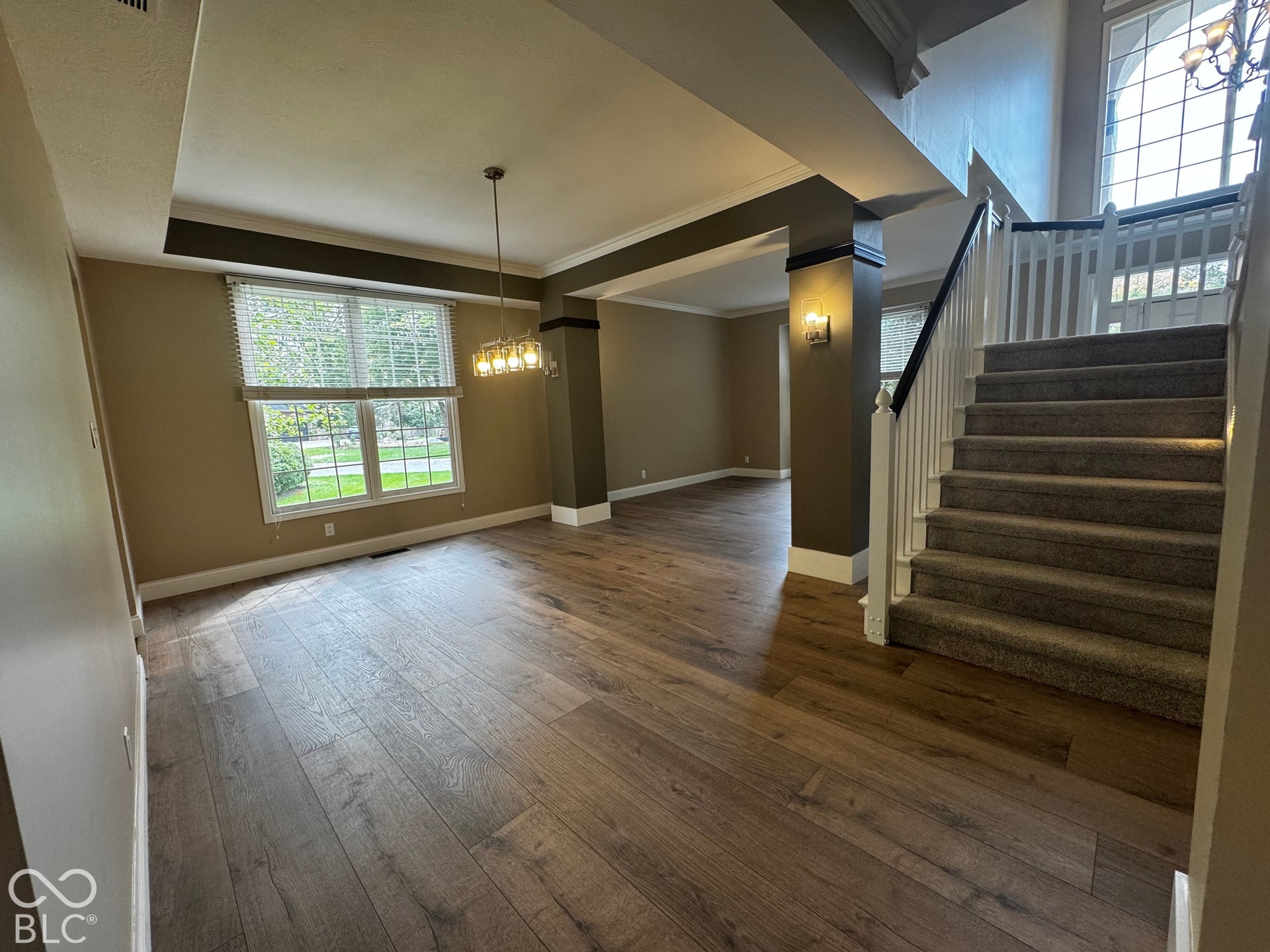 Tray ceiling, wood-finish flooring, two-story window, chandelier lighting, and a carpeted staircase with white balusters