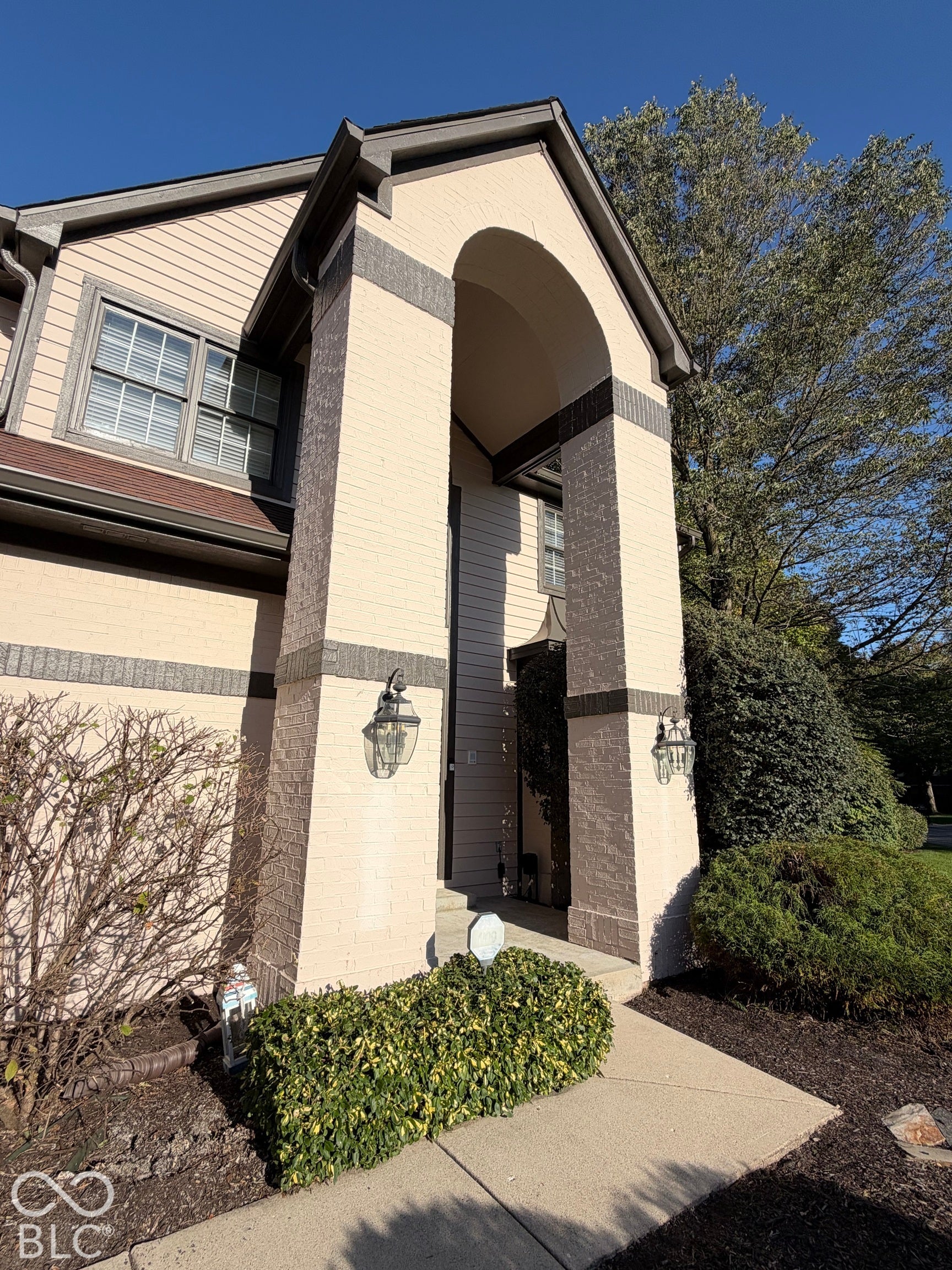 Arched entryway featuring brick and siding facade, concrete walkway, and exterior sconce lighting