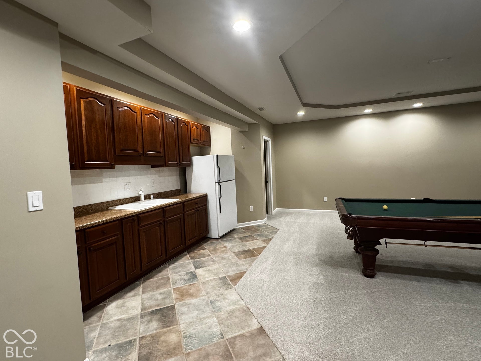 Built-in wet bar with wood-finish cabinetry and stone-look countertop, tile flooring, wall-to-wall carpeting, and recessed lighting