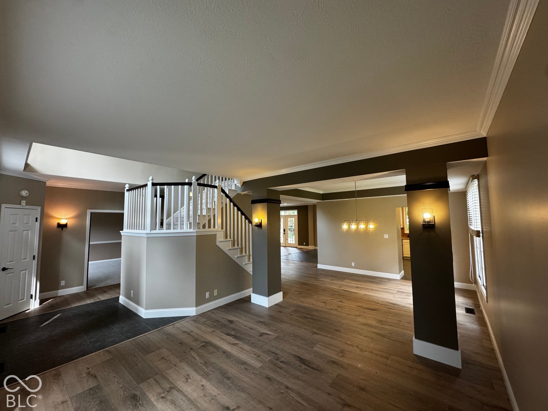 Wood-finish flooring, staircase with white spindles and dark banister, recessed lighting, and wall sconces