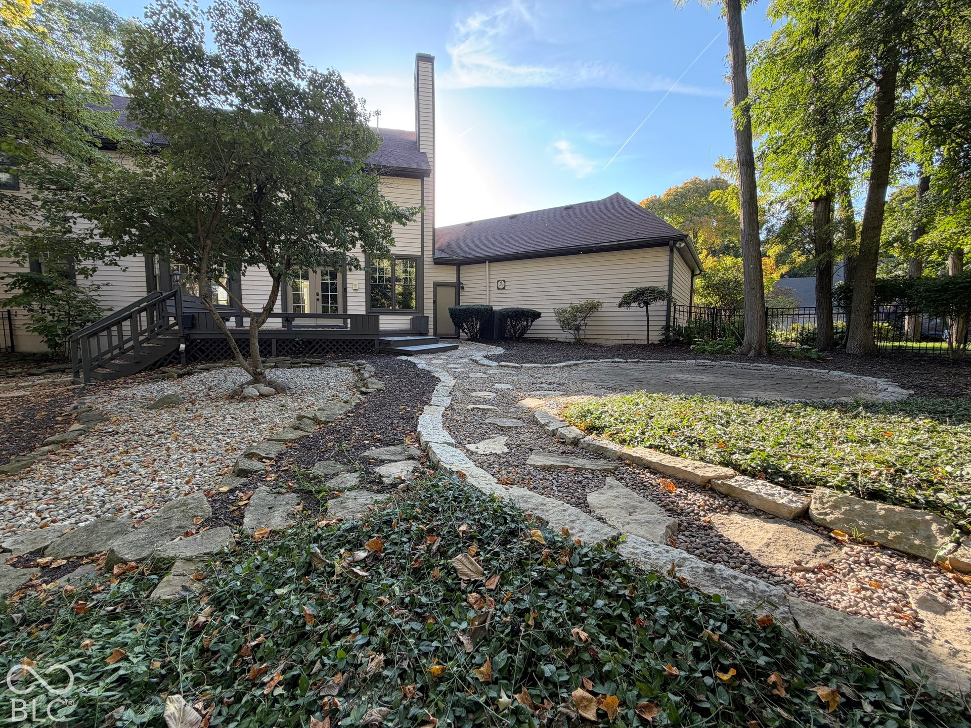 Rear exterior featuring a spacious deck with dark wood railing, stone paver pathway, and mature trees