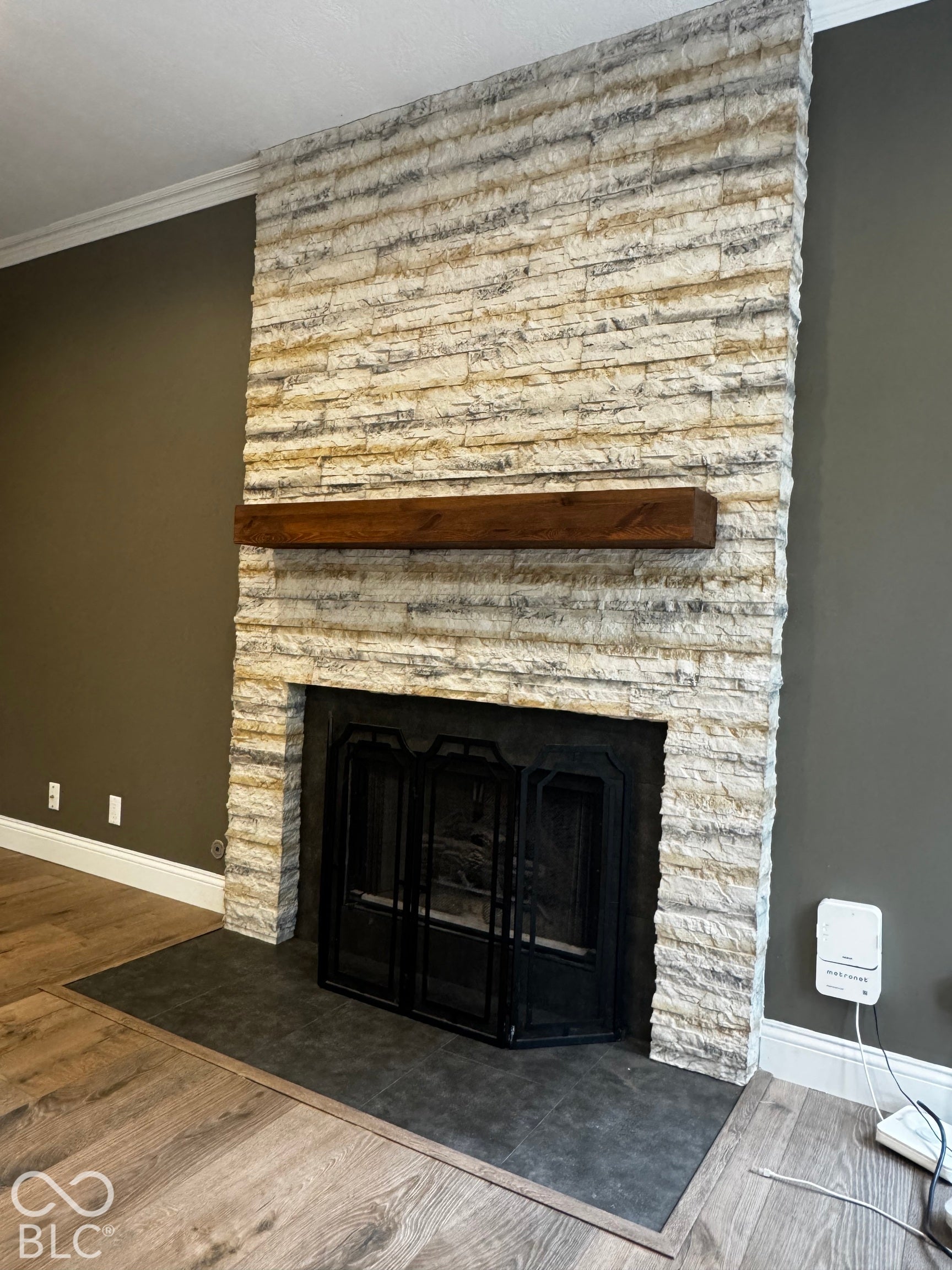 Stone-clad fireplace with a dark wood-finish mantel and a black metal fire screen