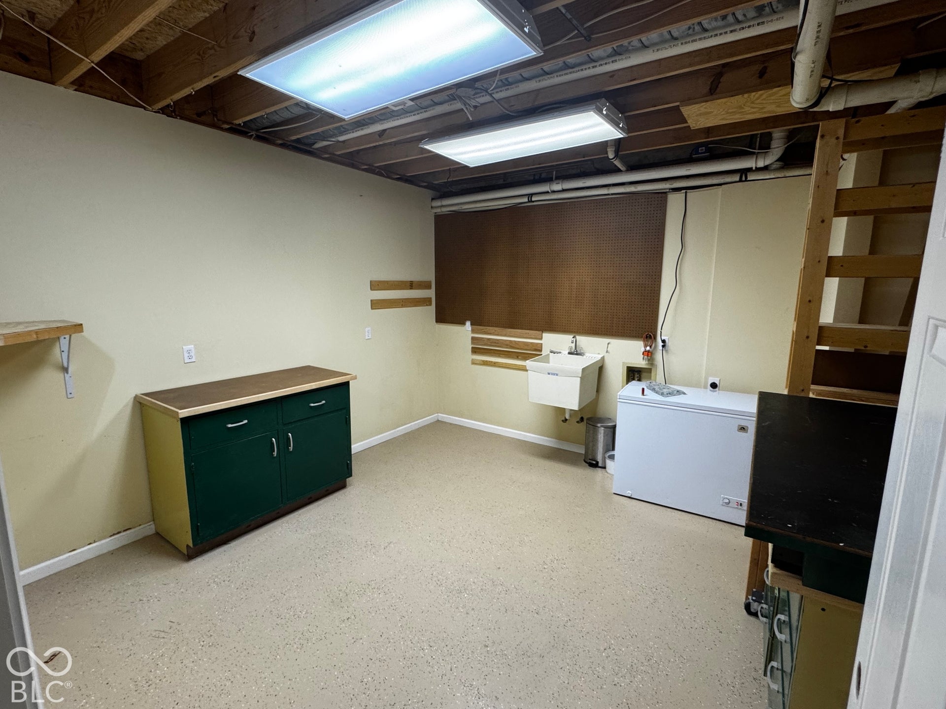 Utility room with exposed ceiling joists, light-colored walls, and a wall-mounted utility sink. Previously used as a "man cave with gun safes, and toys"