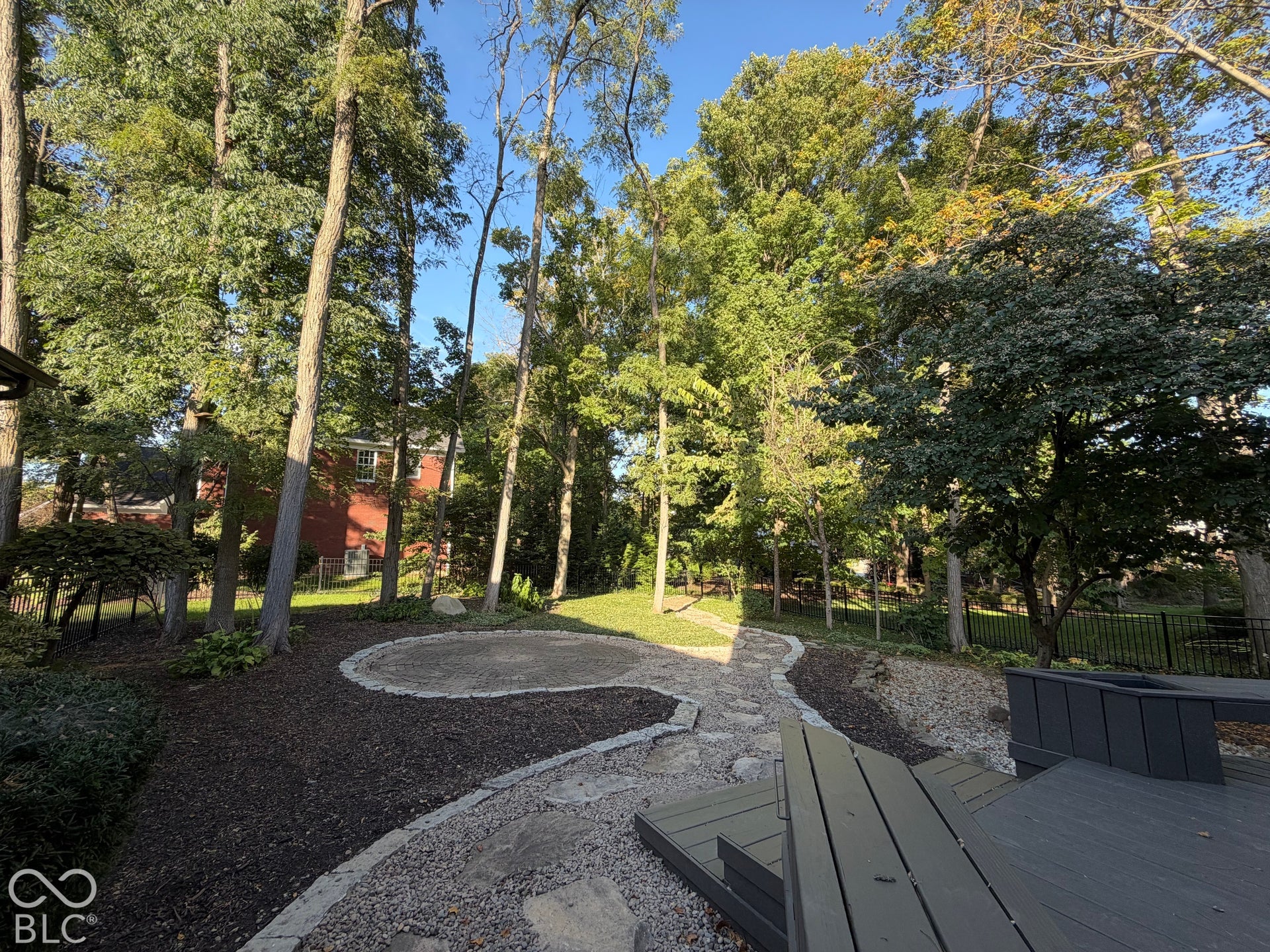 Expansive yard featuring mature trees, a multi-level deck, gravel pathways, and a circular gravel patio area
