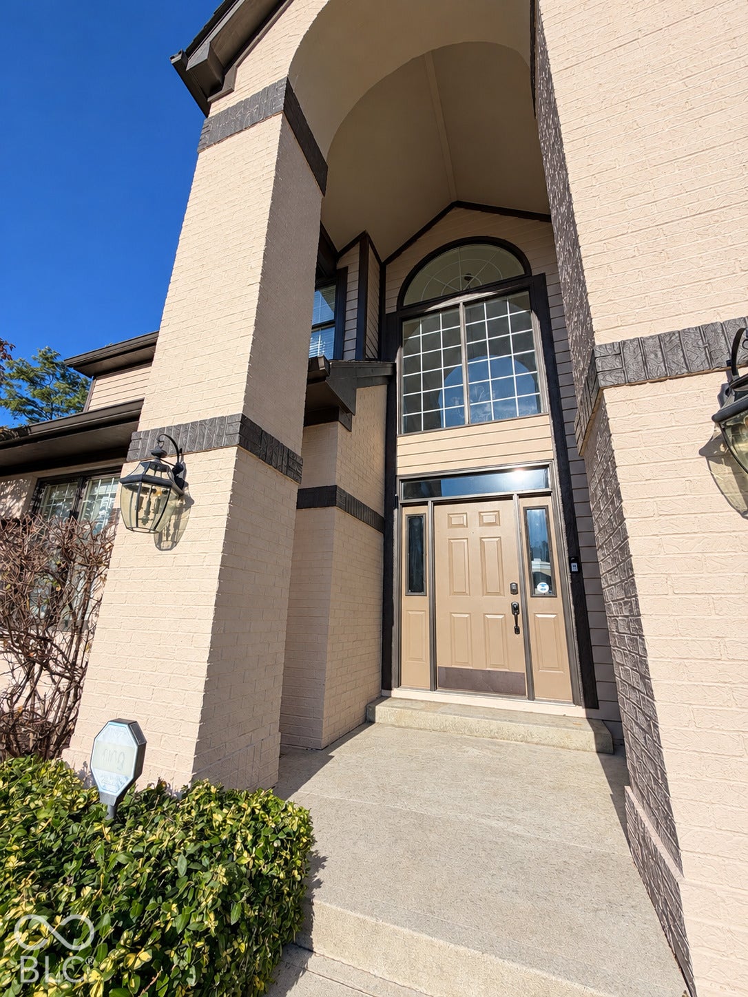 Arched entry with a prominent transom window and sidelights, featuring brick and siding exterior, concrete walkway, and exterior lighting fixtures
