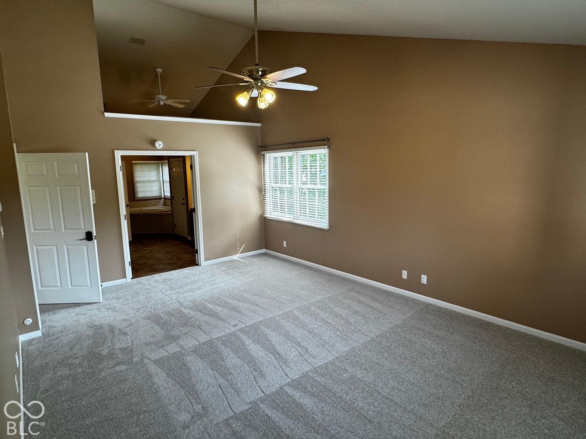Primary bedroom with Vaulted ceiling, light gray patterned carpeting, and white window blinds