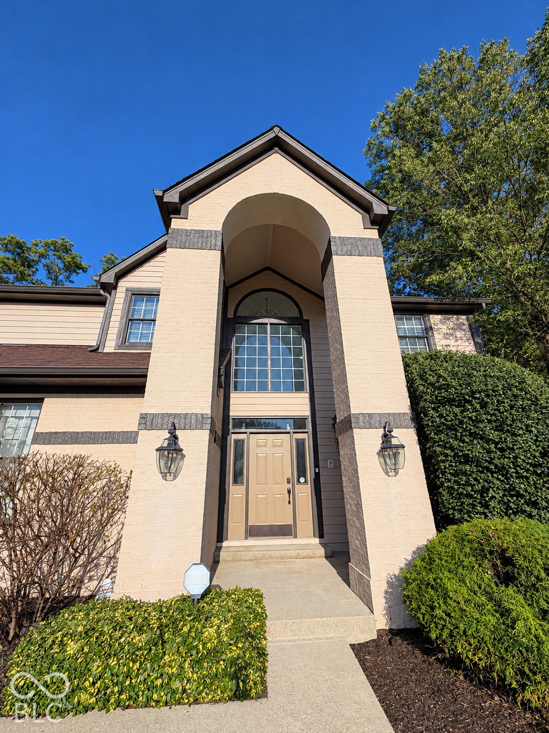 Arched entry with a transom window above the front door, flanked by two exterior wall sconces, and a concrete walkway