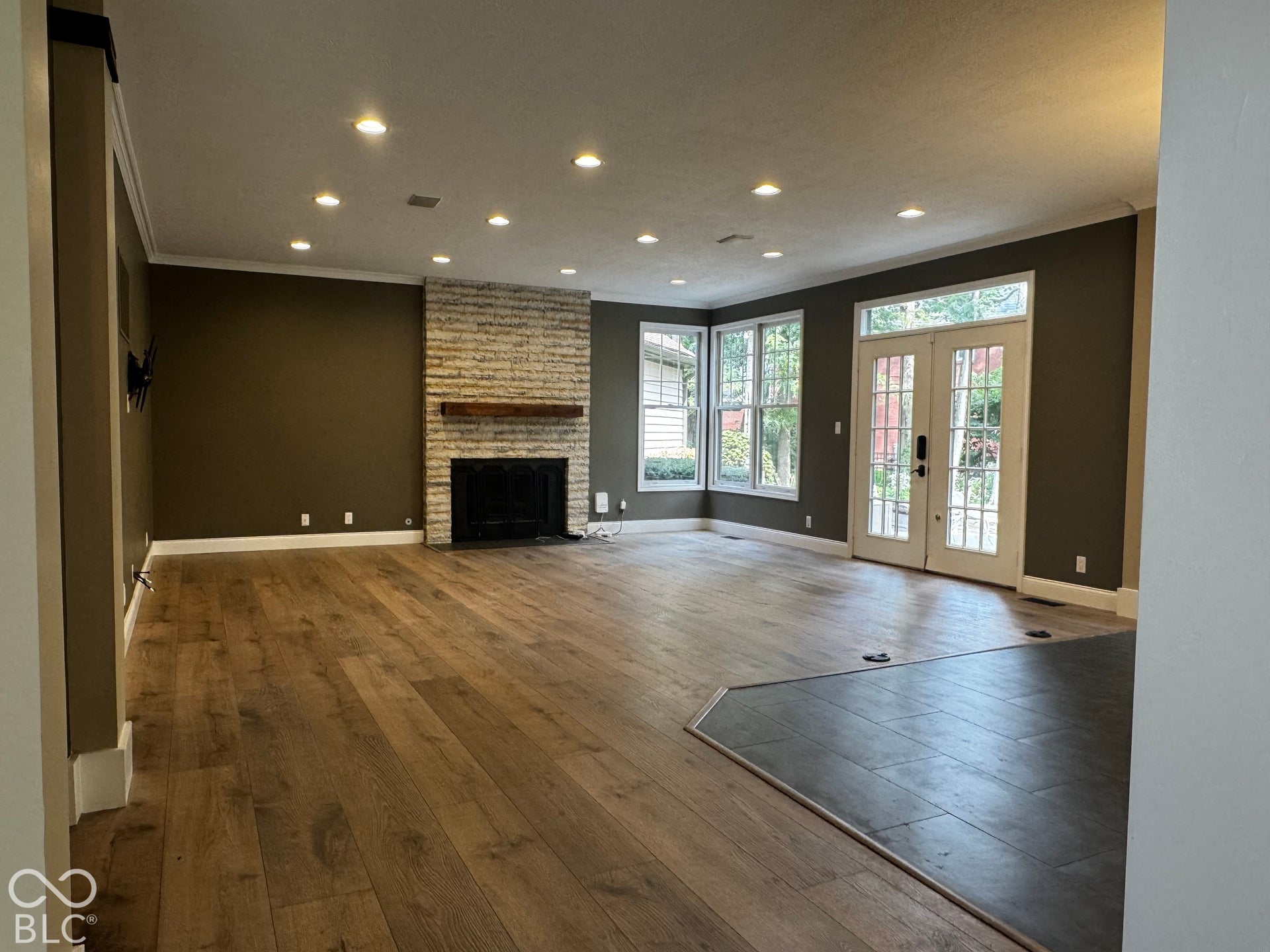 Recessed lighting, wood-finish flooring, stone-clad fireplace with wood mantel, multiple windows, and French doors