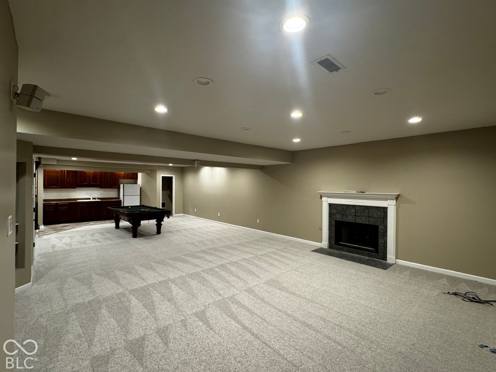 Expansive carpeted room featuring recessed lighting, a built-in fireplace with a stone surround, and a wet bar with wood cabinetry and a sink