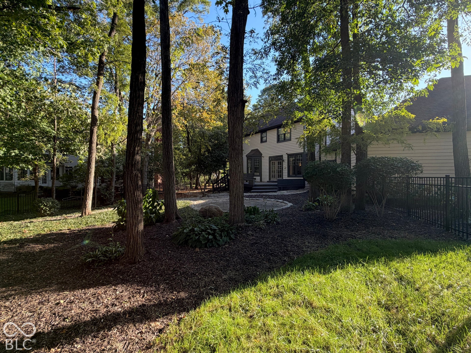 Rear exterior featuring a stone patio, mature trees, and a decorative metal fence