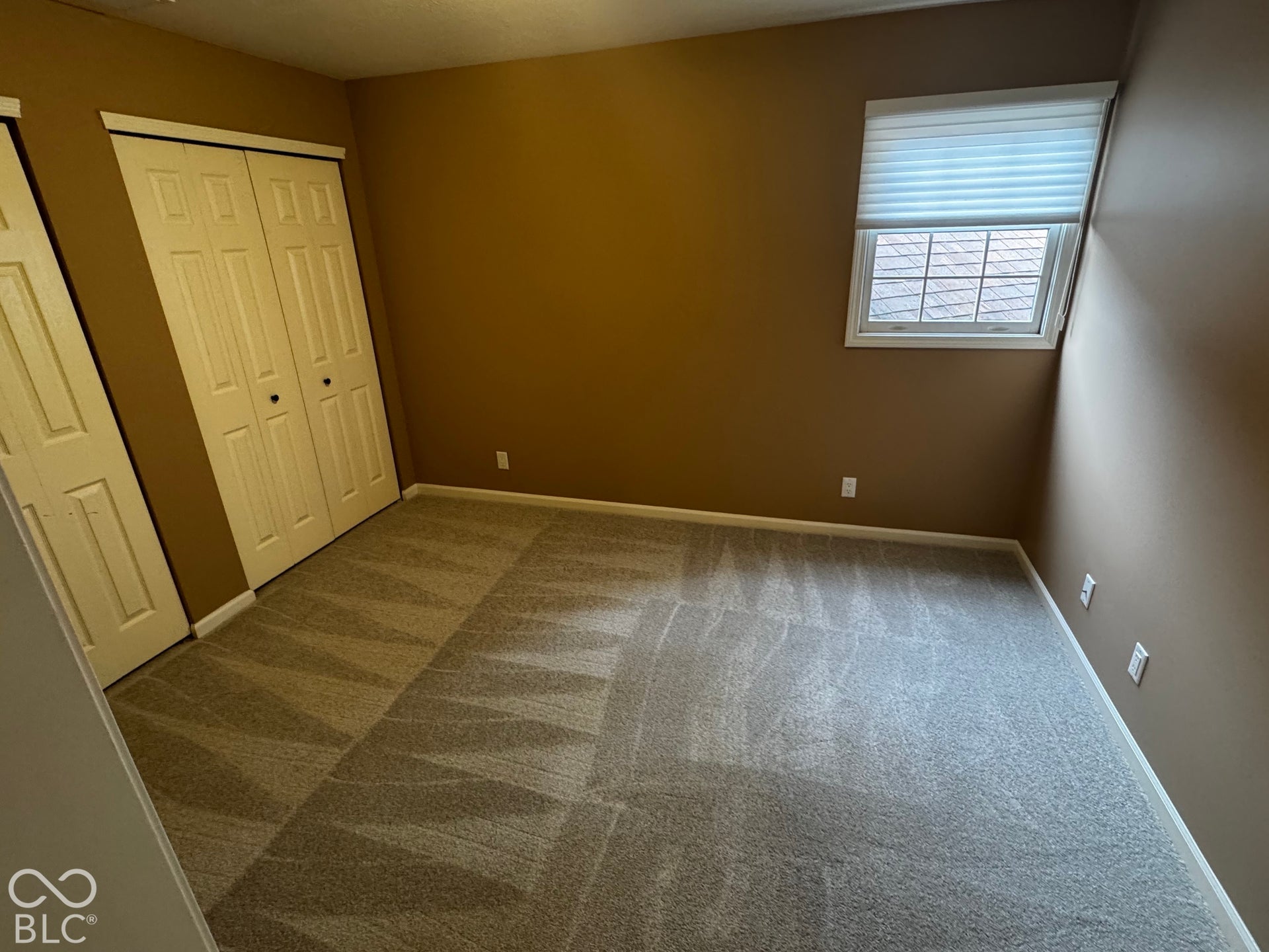 Carpeted room featuring a window with cellular shades and white trim, and bi-fold closet doors