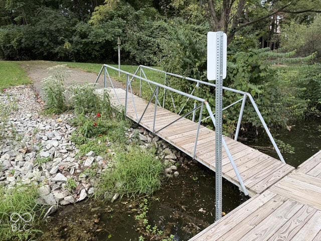 Wooden footbridge with metal railings over a channel, leading to a gravel path