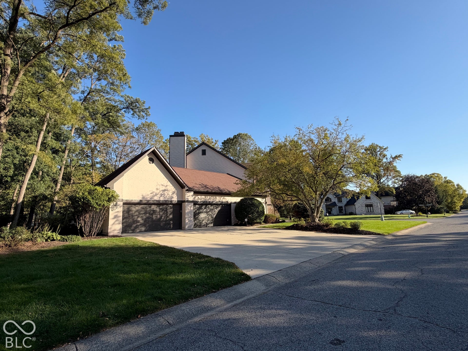 Stucco exterior with a peaked roofline, multiple garage doors, and mature trees surrounding the property