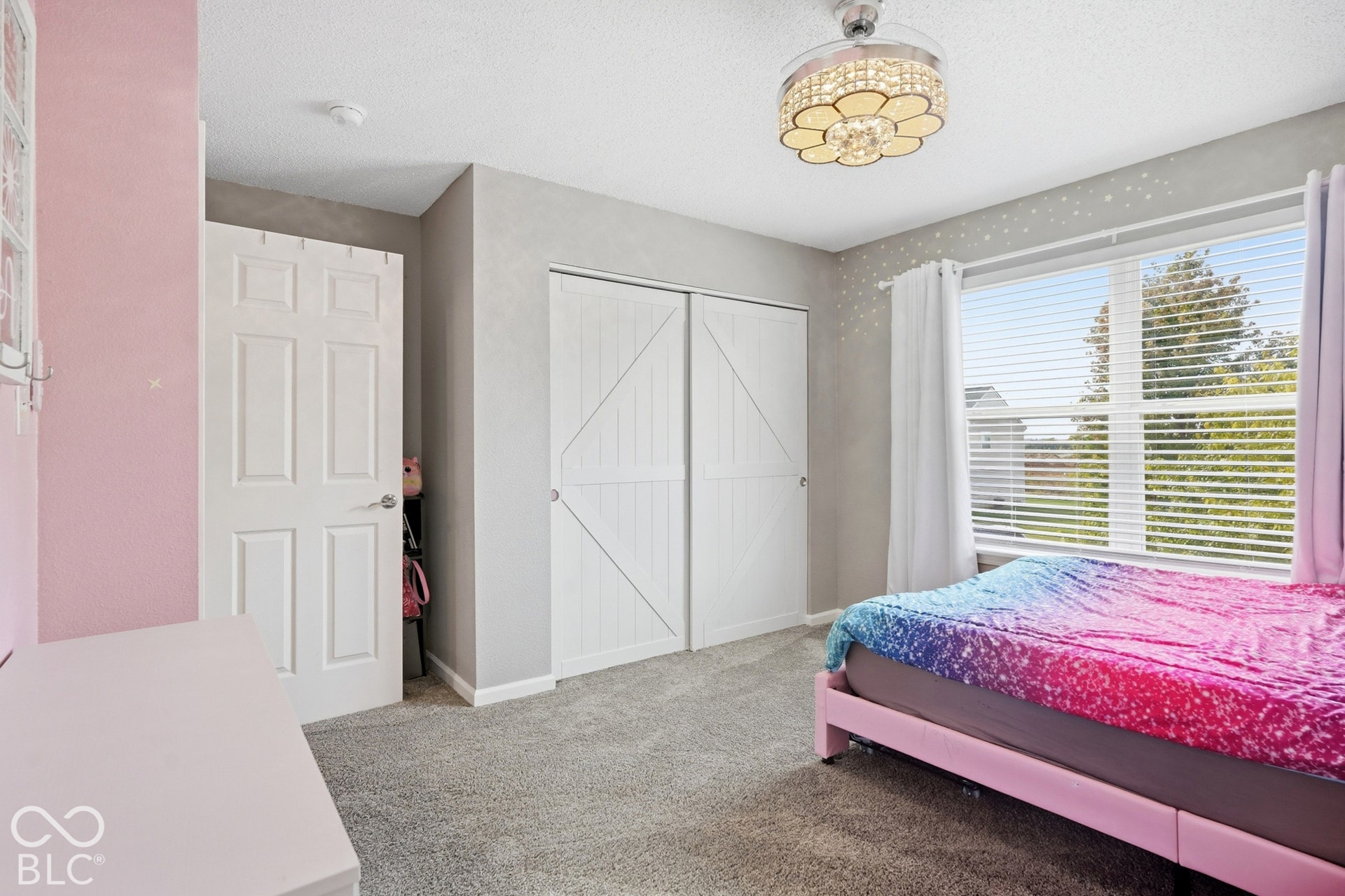 Ceiling fan with decorative light fixture, carpeted flooring, large window with blinds, and white bi-fold closet doors